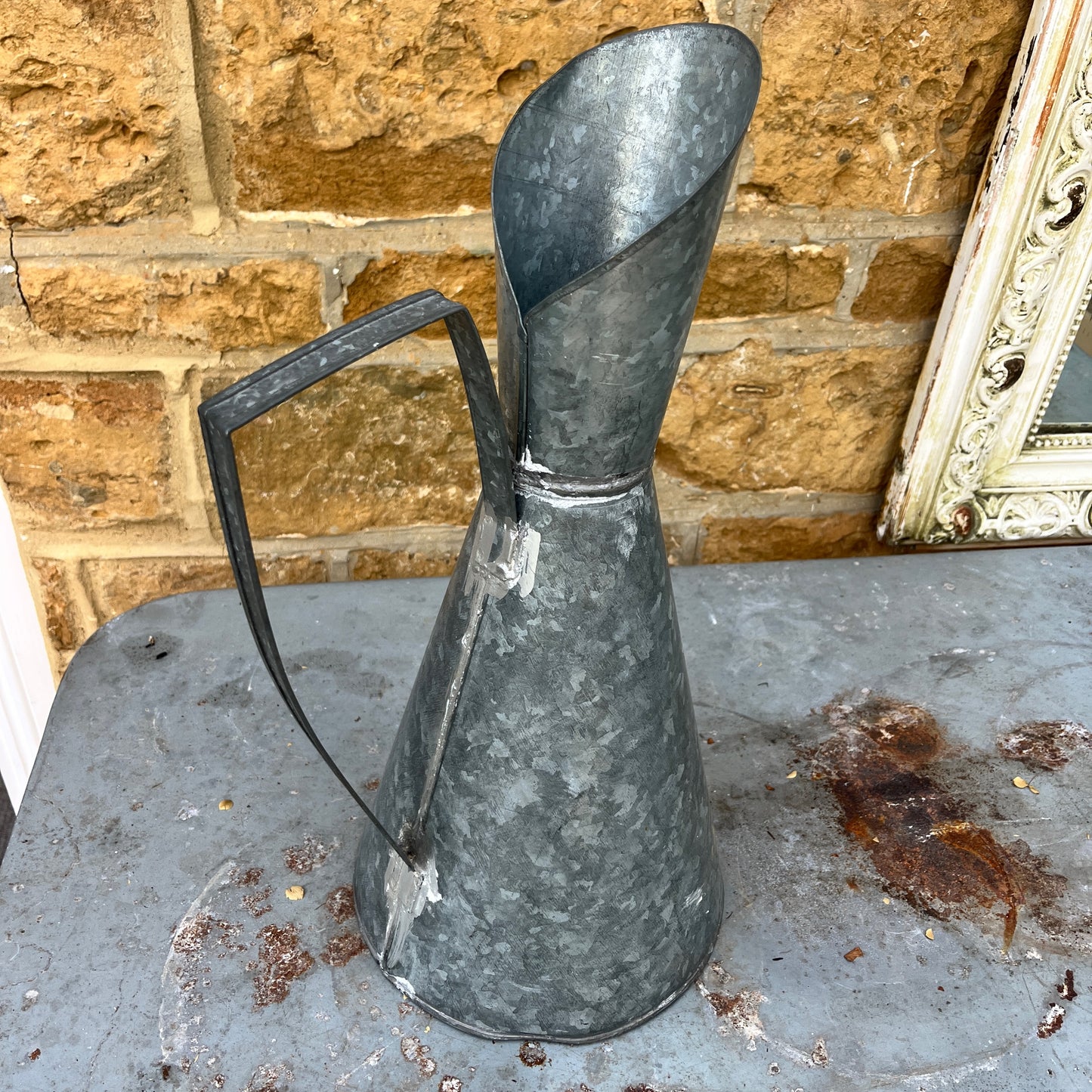 An elegant galvanized jug with a sleek, silver finish, featuring a stylized design with a gracefully curved handle and a flared spout