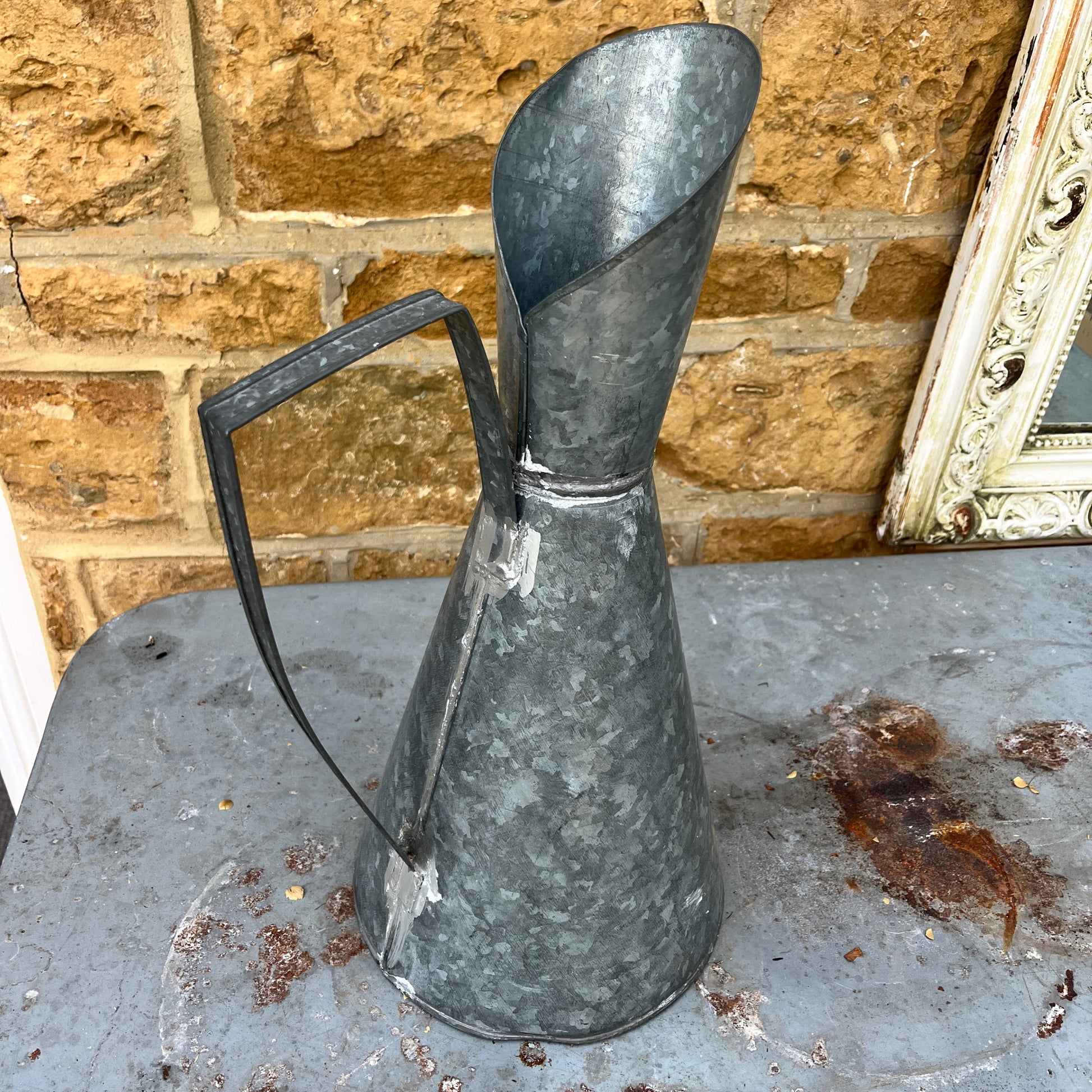 An elegant galvanized jug with a sleek, silver finish, featuring a stylized design with a gracefully curved handle and a flared spout