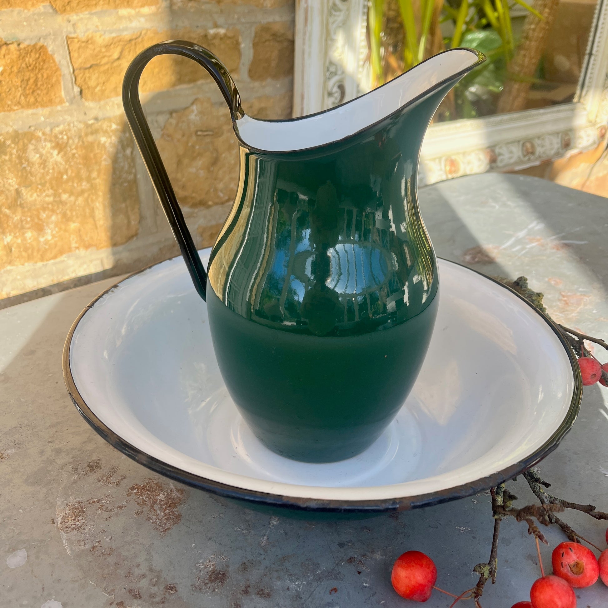 Green enamel jug and bowl set with a white interior and black detailing along the rims. The pieces feature a vintage, rustic design with a glossy finish, evoking classic enamelware style.