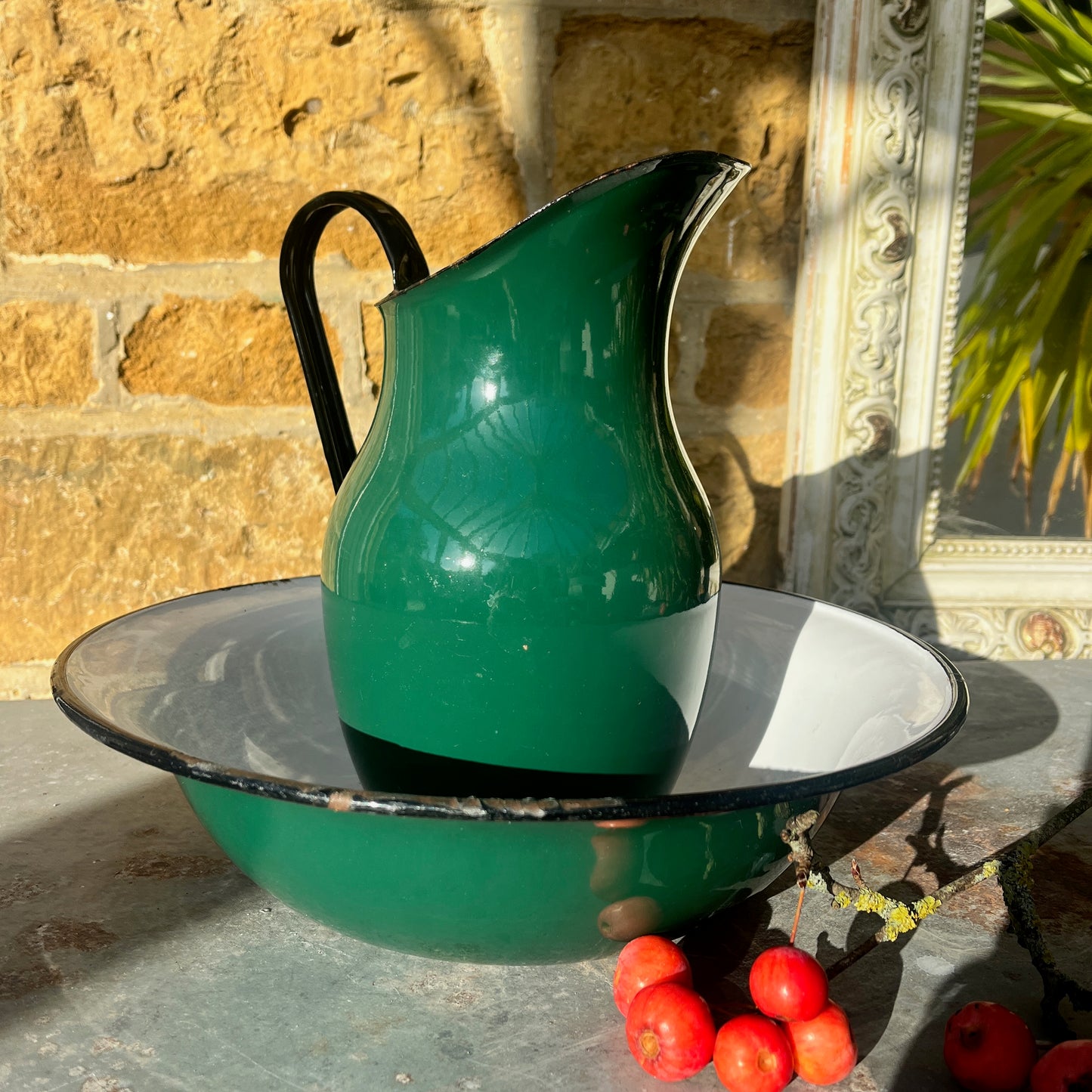 Green enamel jug and bowl set with a white interior and black detailing along the rims. The pieces feature a vintage, rustic design with a glossy finish, evoking classic enamelware style.