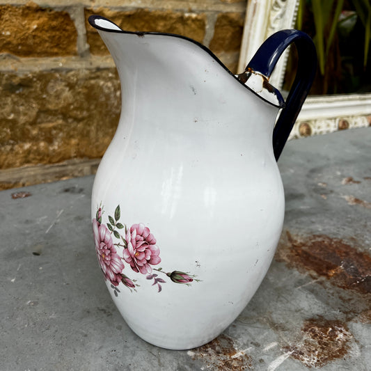 A vintage white enamel jug with a gently curved shape and sturdy handle, decorated with a delicate floral pattern in soft pinks and greens