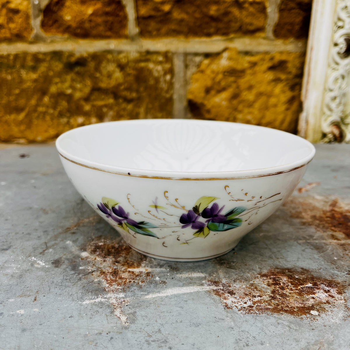 A vintage white ceramic bowl with a floral purple and green pattern.