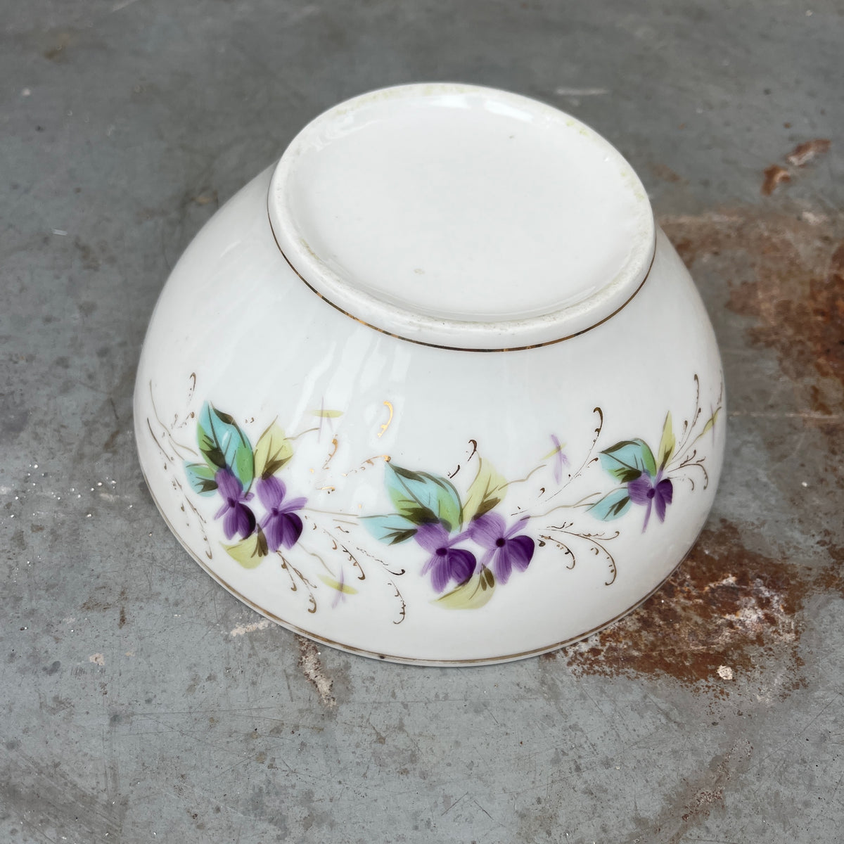 A vintage white ceramic bowl with a floral purple and green pattern.