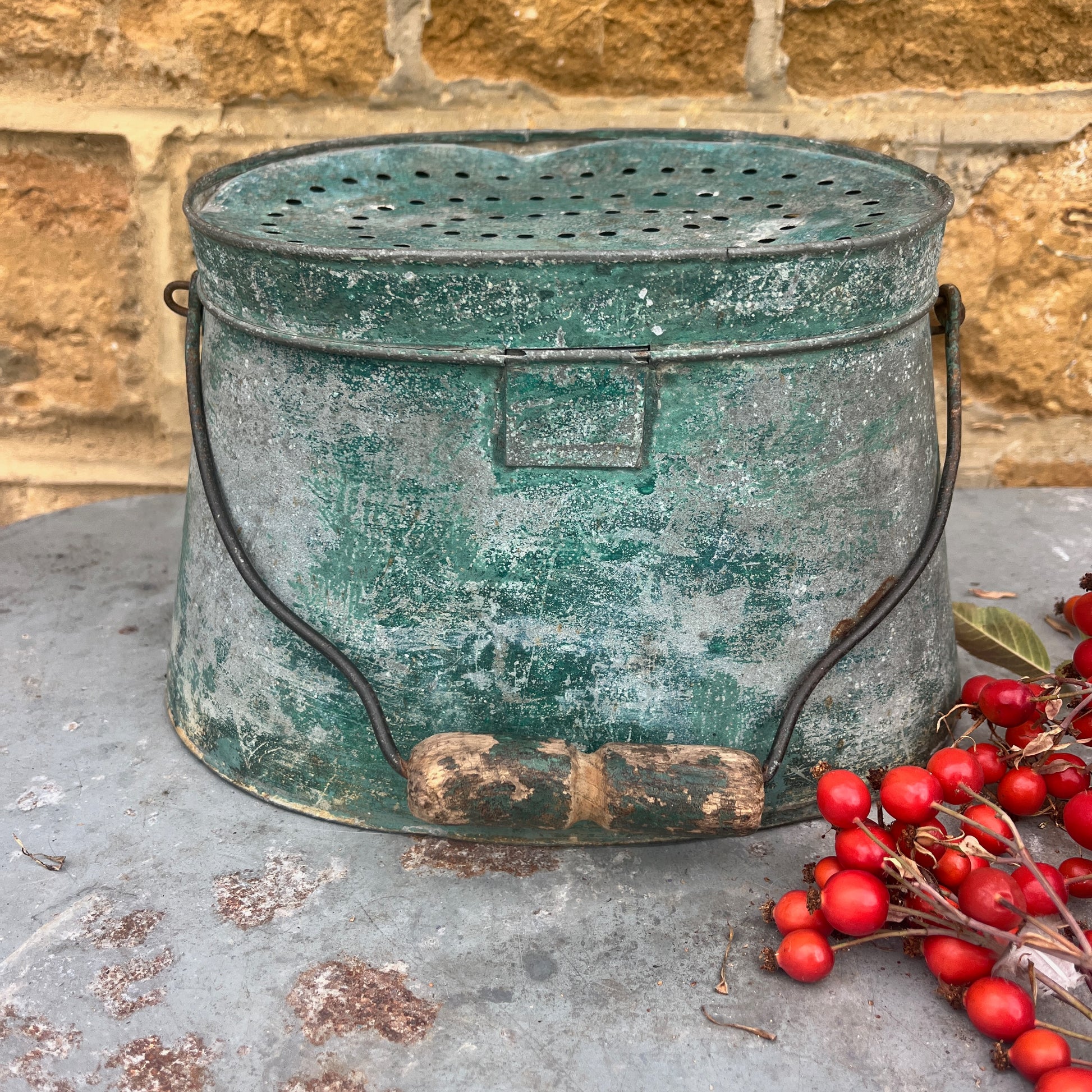 Vintage green metal container with red berries on a stone surface