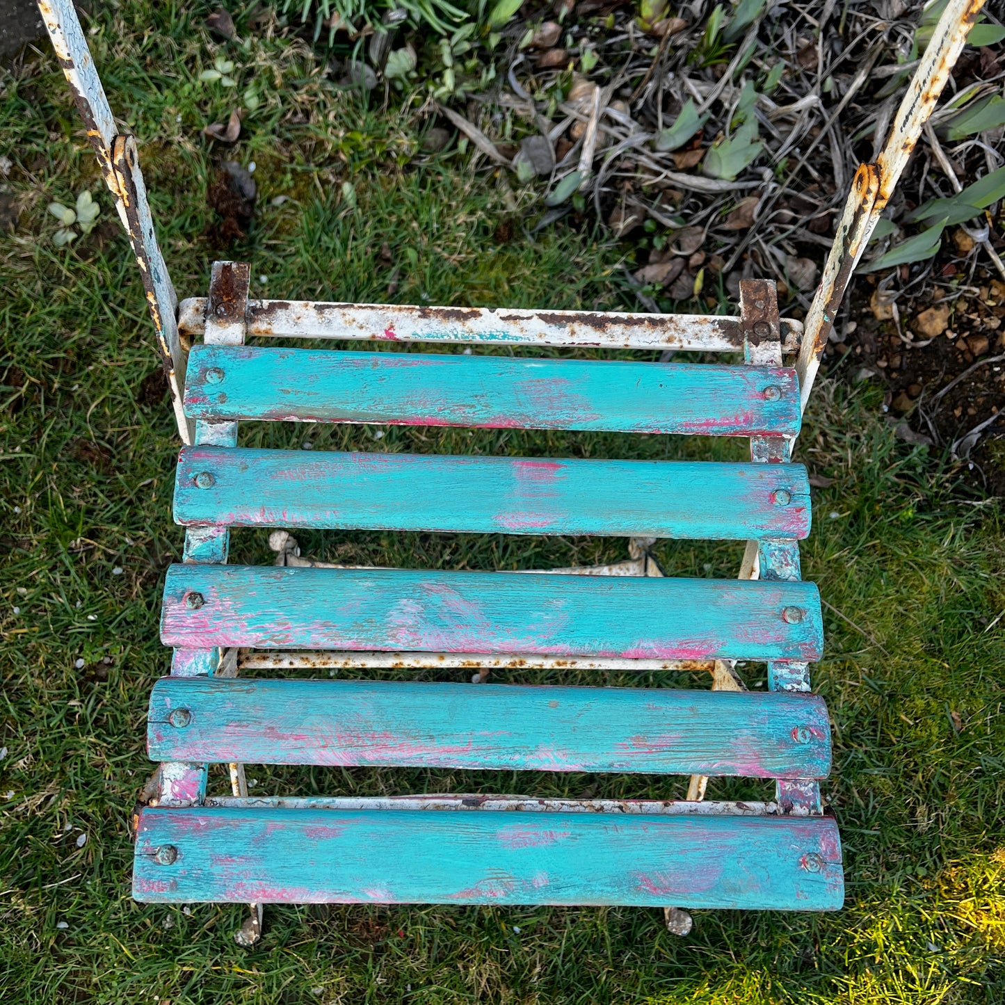Vintage French bistro chairs with wooden slatted seats and backs, featuring metal folding frames painted in turquoise and pink.
