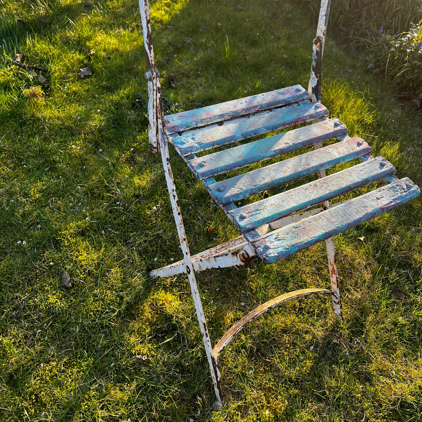 Vintage French bistro chairs with wooden slatted seats and backs, featuring metal folding frames painted in turquoise and pink.
