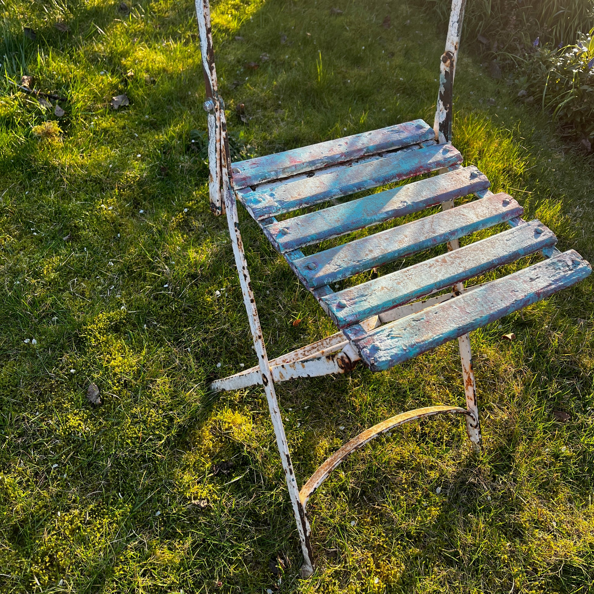 Vintage French bistro chairs with wooden slatted seats and backs, featuring metal folding frames painted in turquoise and pink.
