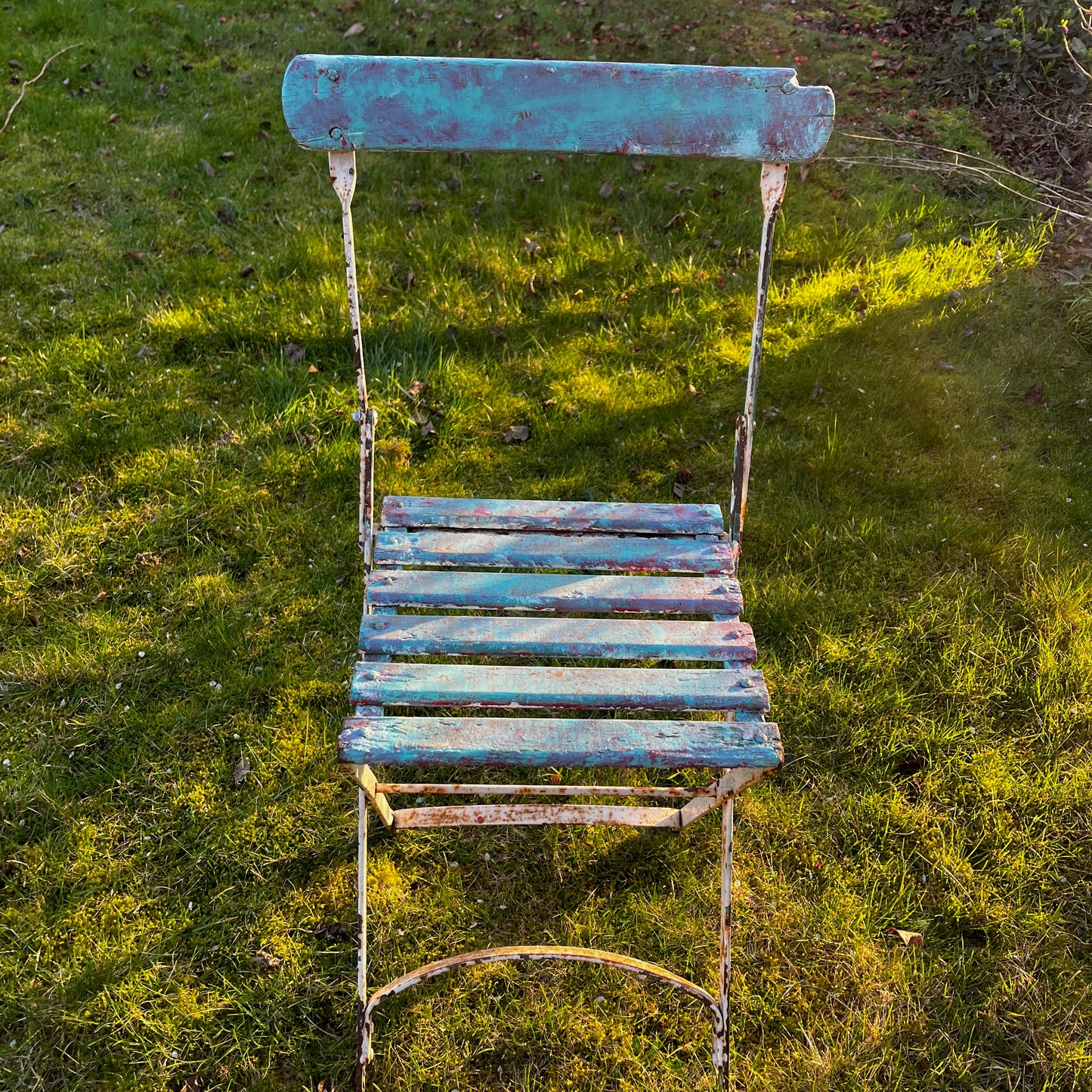 Vintage French bistro chairs with wooden slatted seats and backs, featuring metal folding frames painted in turquoise and pink.
