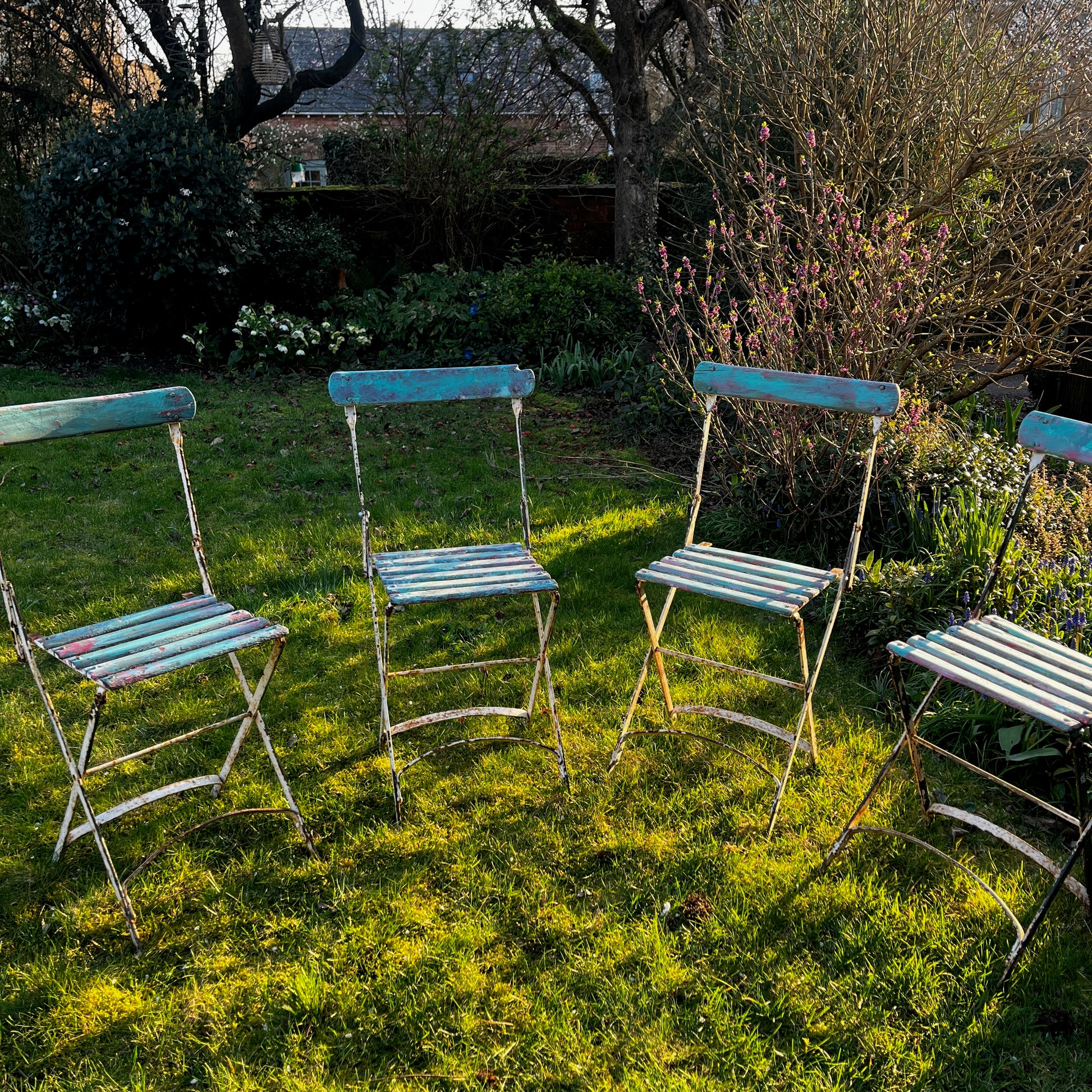 Vintage French bistro chairs with wooden slatted seats and backs, featuring metal folding frames painted in turquoise and pink.
