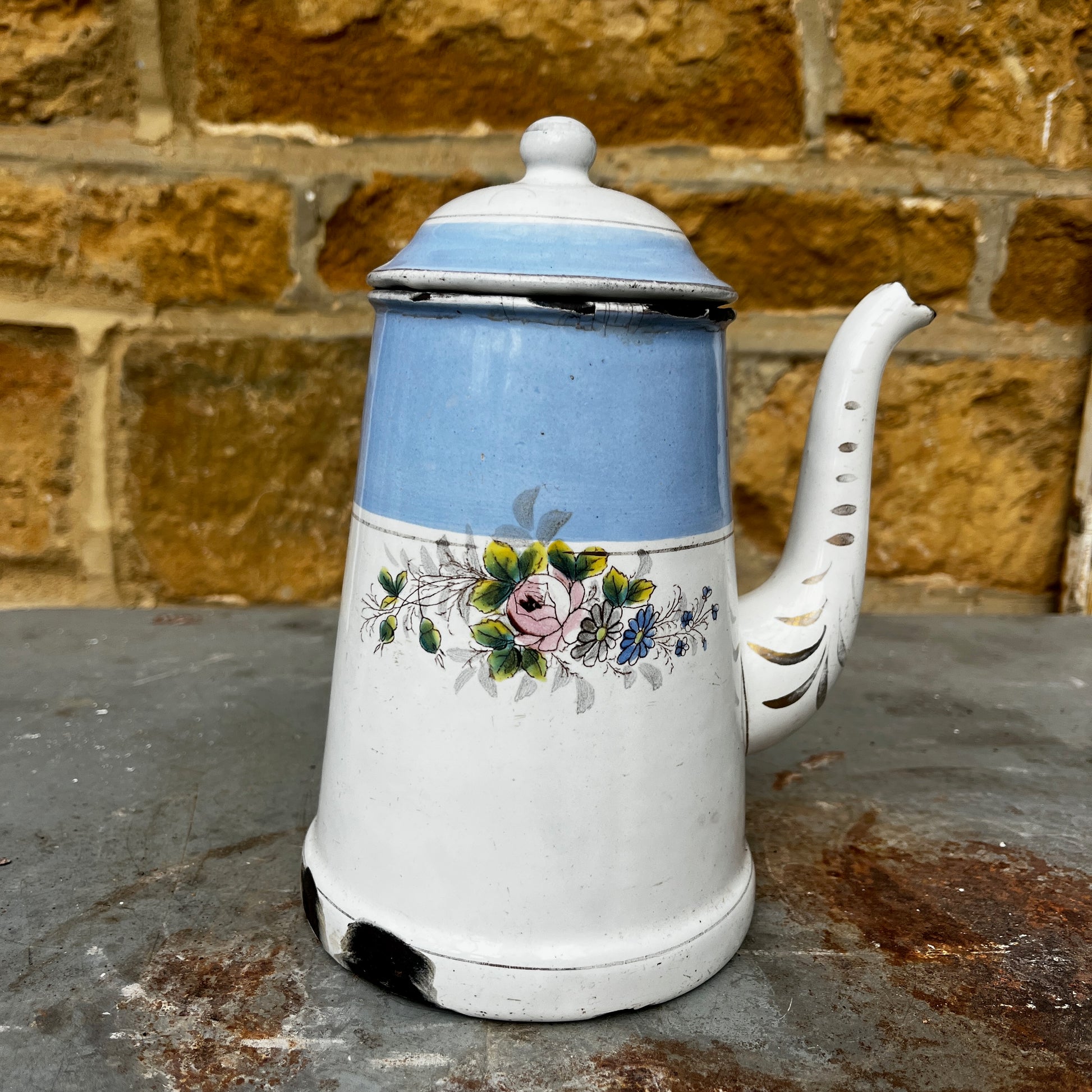 An antique austro-hungarian enamel coffee pot with a light blue upper body, white lower body, and a floral rose pattern, and brown wooden handle.