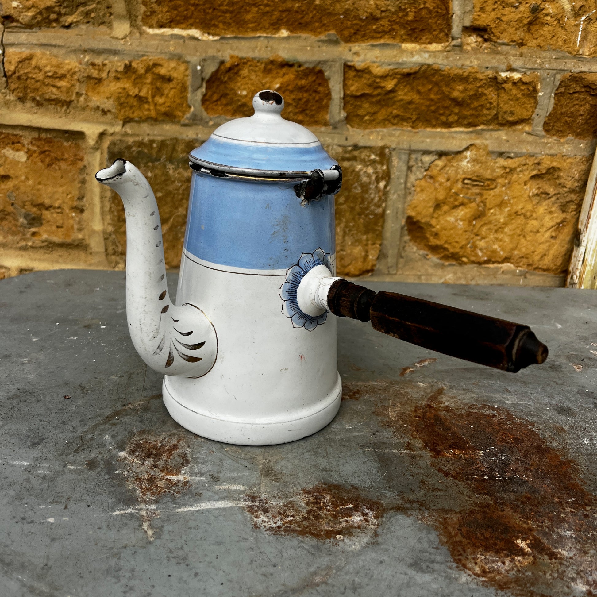 An antique austro-hungarian enamel coffee pot with a light blue upper body, white lower body, and a floral rose pattern, and brown wooden handle.