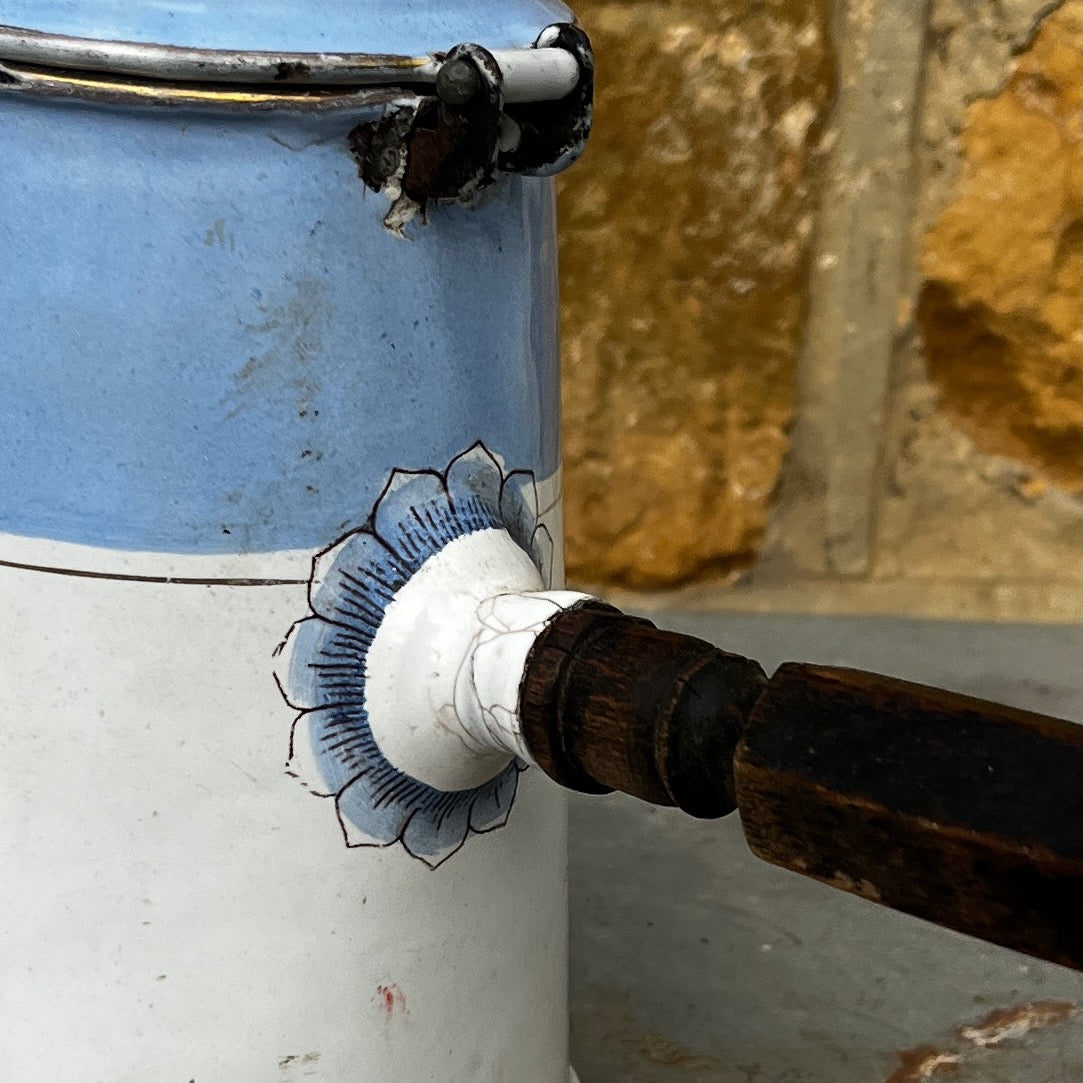 An antique austro-hungarian enamel coffee pot with a light blue upper body, white lower body, and a floral rose pattern, and brown wooden handle.
