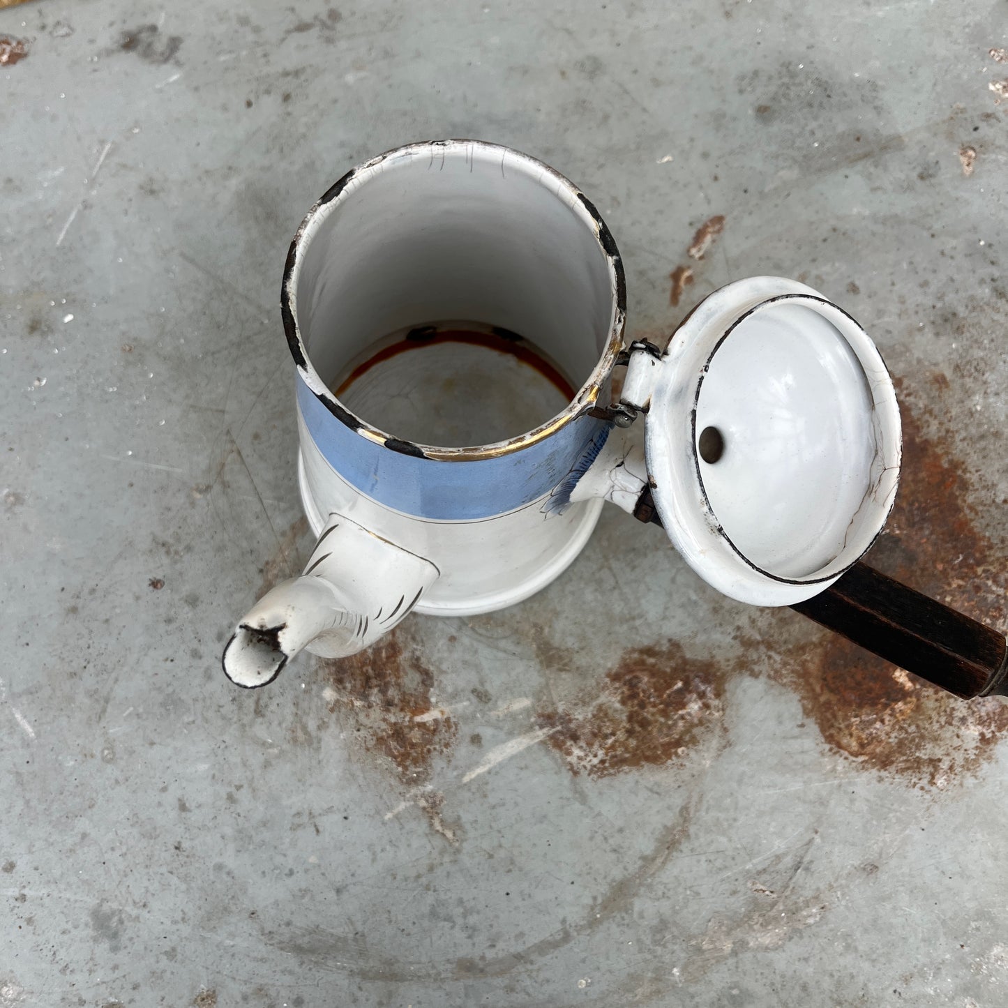An antique austro-hungarian enamel coffee pot with a light blue upper body, white lower body, and a floral rose pattern, and brown wooden handle.