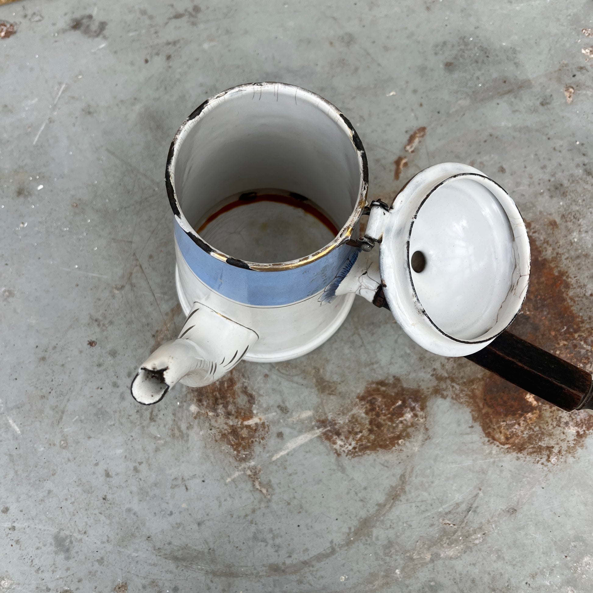 An antique austro-hungarian enamel coffee pot with a light blue upper body, white lower body, and a floral rose pattern, and brown wooden handle.