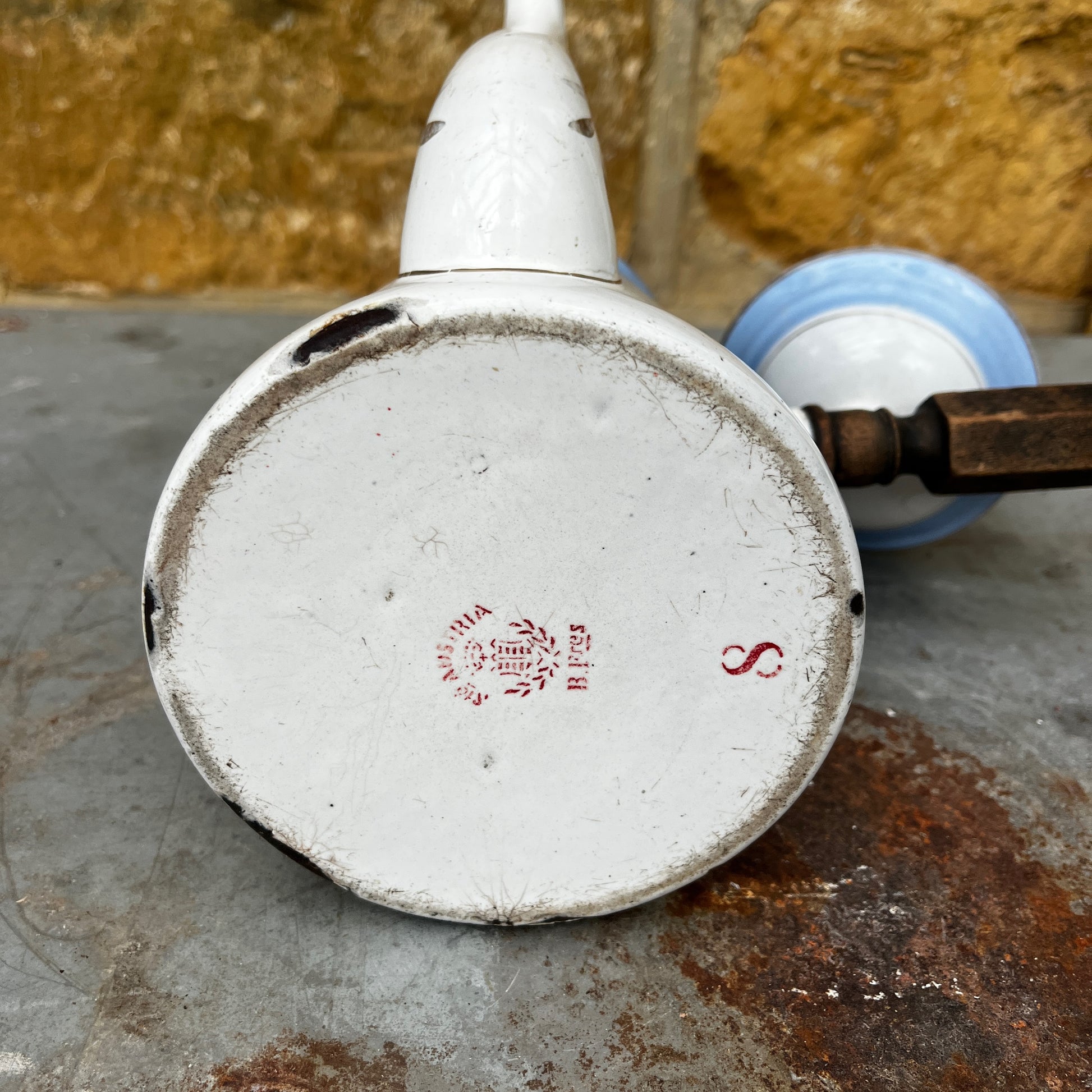 An antique austro-hungarian enamel coffee pot with a light blue upper body, white lower body, and a floral rose pattern, and brown wooden handle.