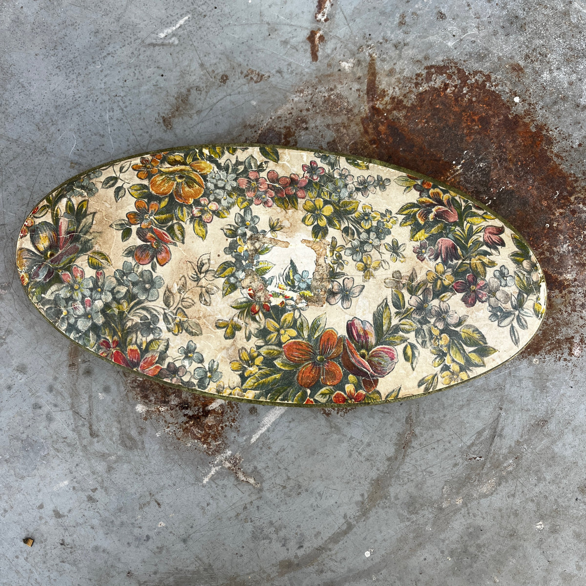An oval vintage cardboard chocolate box with a colorful floral pattern.