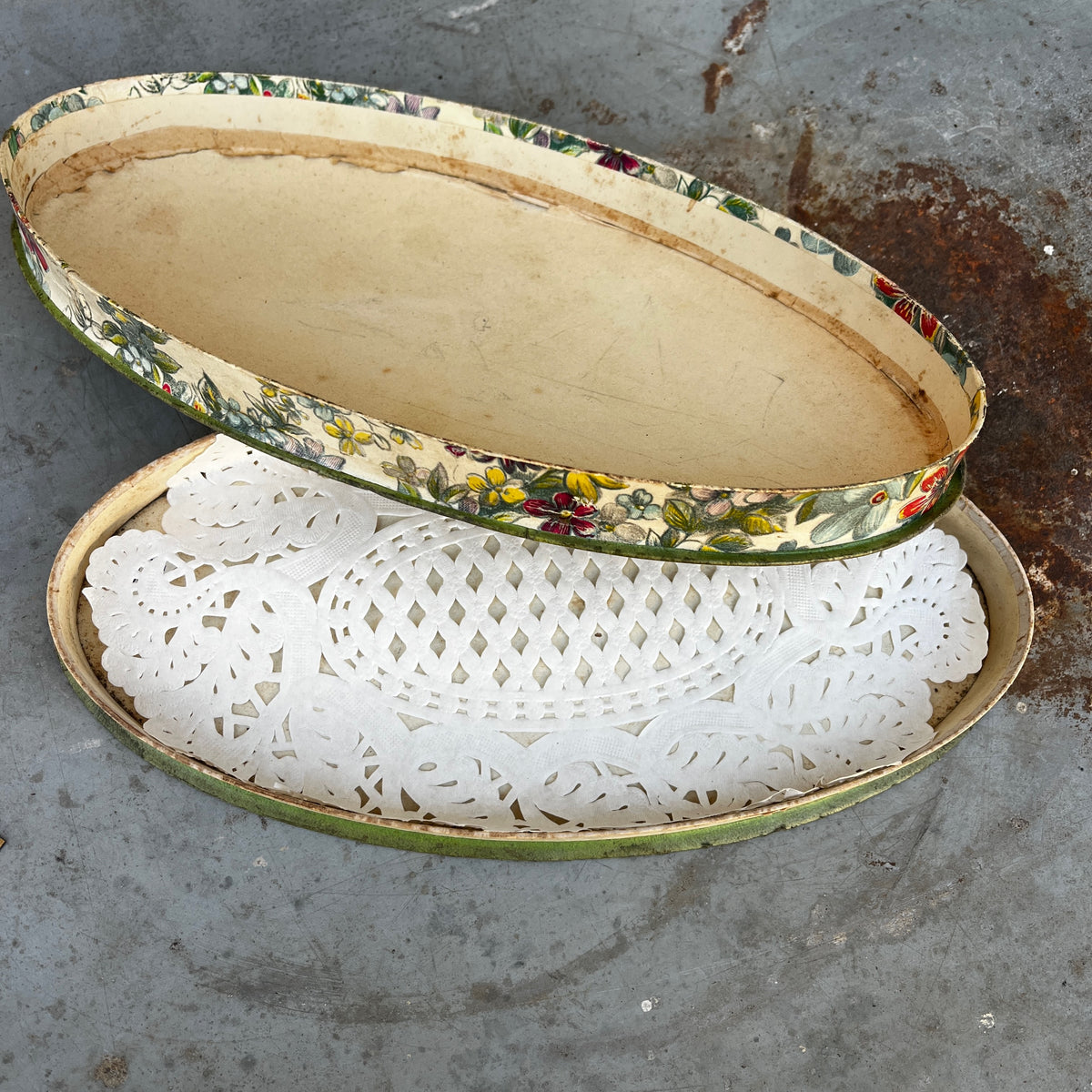 An oval vintage cardboard chocolate box with a colorful floral pattern.