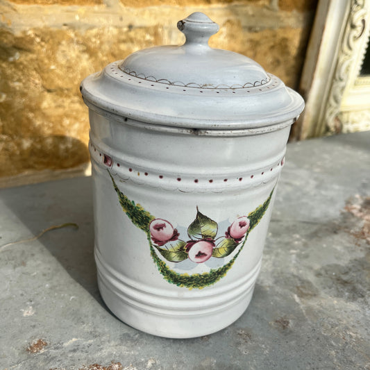 A vintage French enamel canister with a glossy white finish, adorned with intricate gold detailing and a colorful floral pattern on the front.
