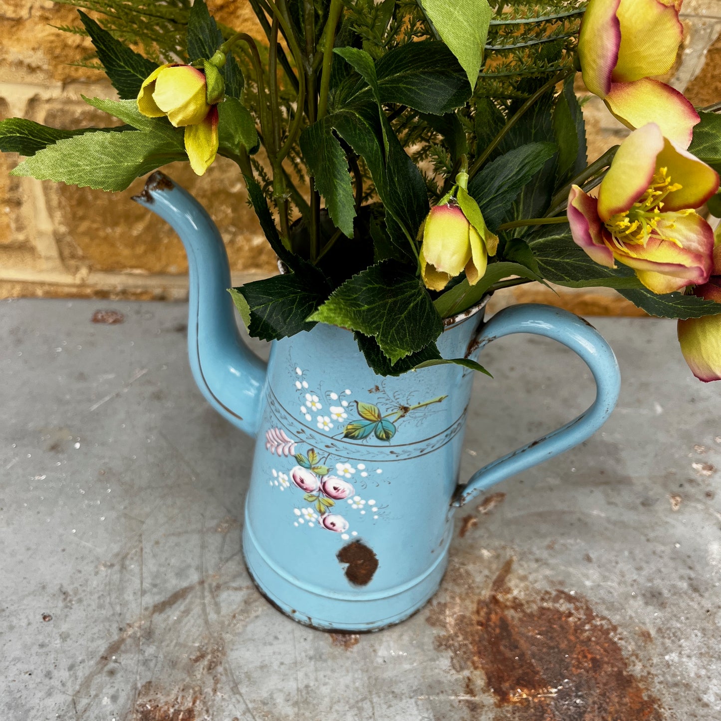 A vintage French enamel jug with a charming floral pattern in soft pink, green, and white tones on a light blue enamel background.