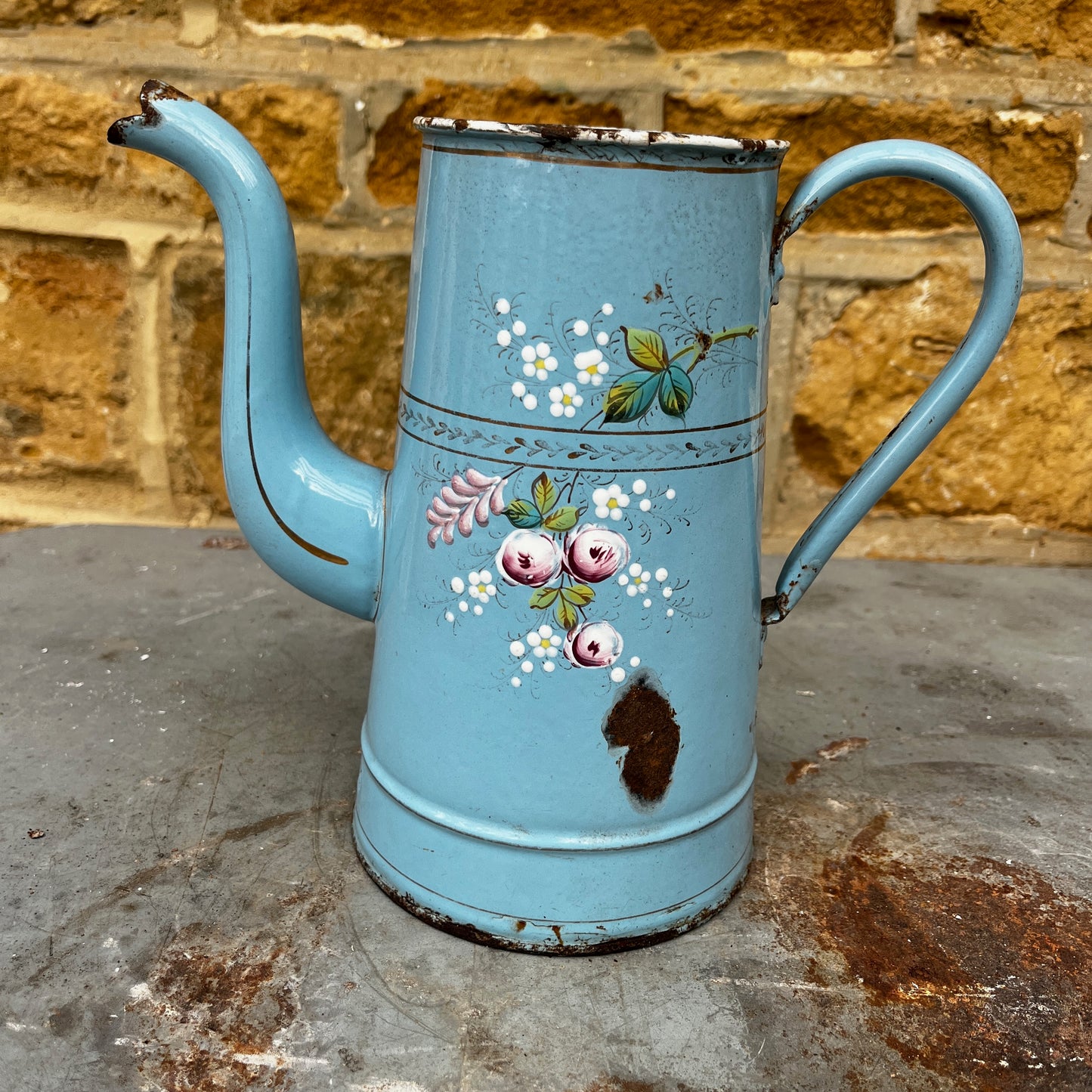 A vintage French enamel jug with a charming floral pattern in soft pink, green, and white tones on a light blue enamel background.