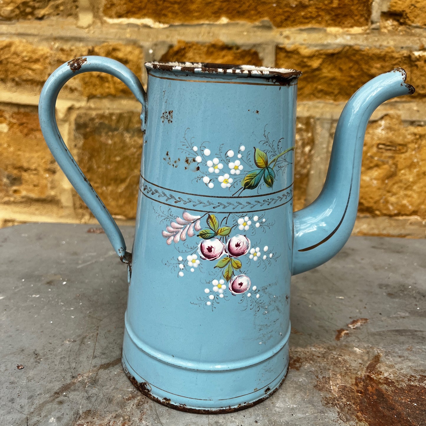 A vintage French enamel jug with a charming floral pattern in soft pink, green, and white tones on a light blue enamel background.