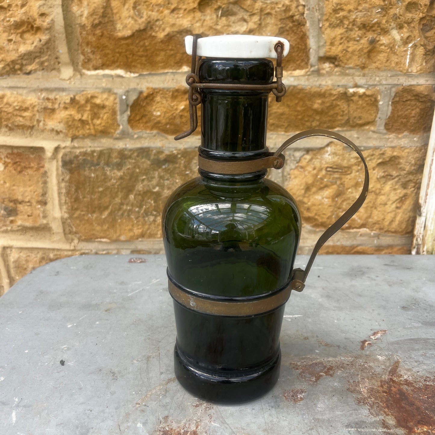 An antique French green glass bottle with a rounded body, ceramic swing-top stopper, and aged metal carry handle