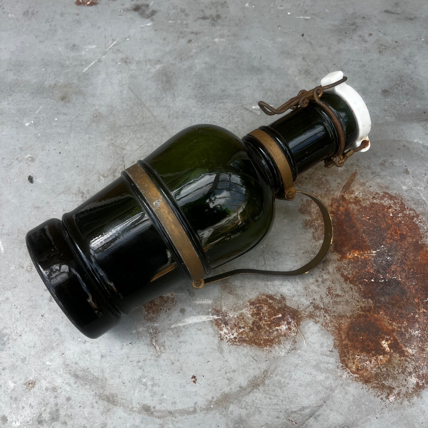 An antique French green glass bottle with a rounded body, ceramic swing-top stopper, and aged metal carry handle