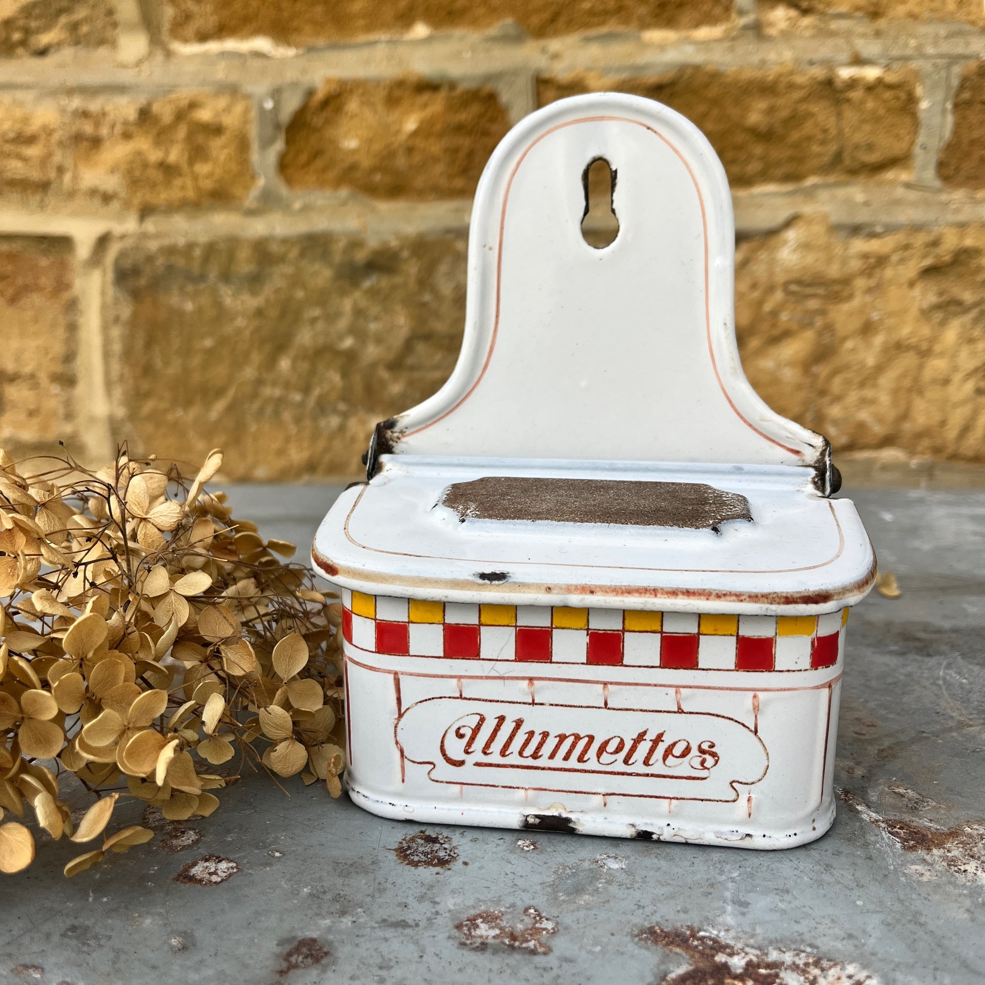 A vintage enamel allumettes box with a white background and red & yellow hand-painted geometric pattern, featuring a chippy weathered finish. The small, rectangular box has a hinged lid, exuding classic French charm