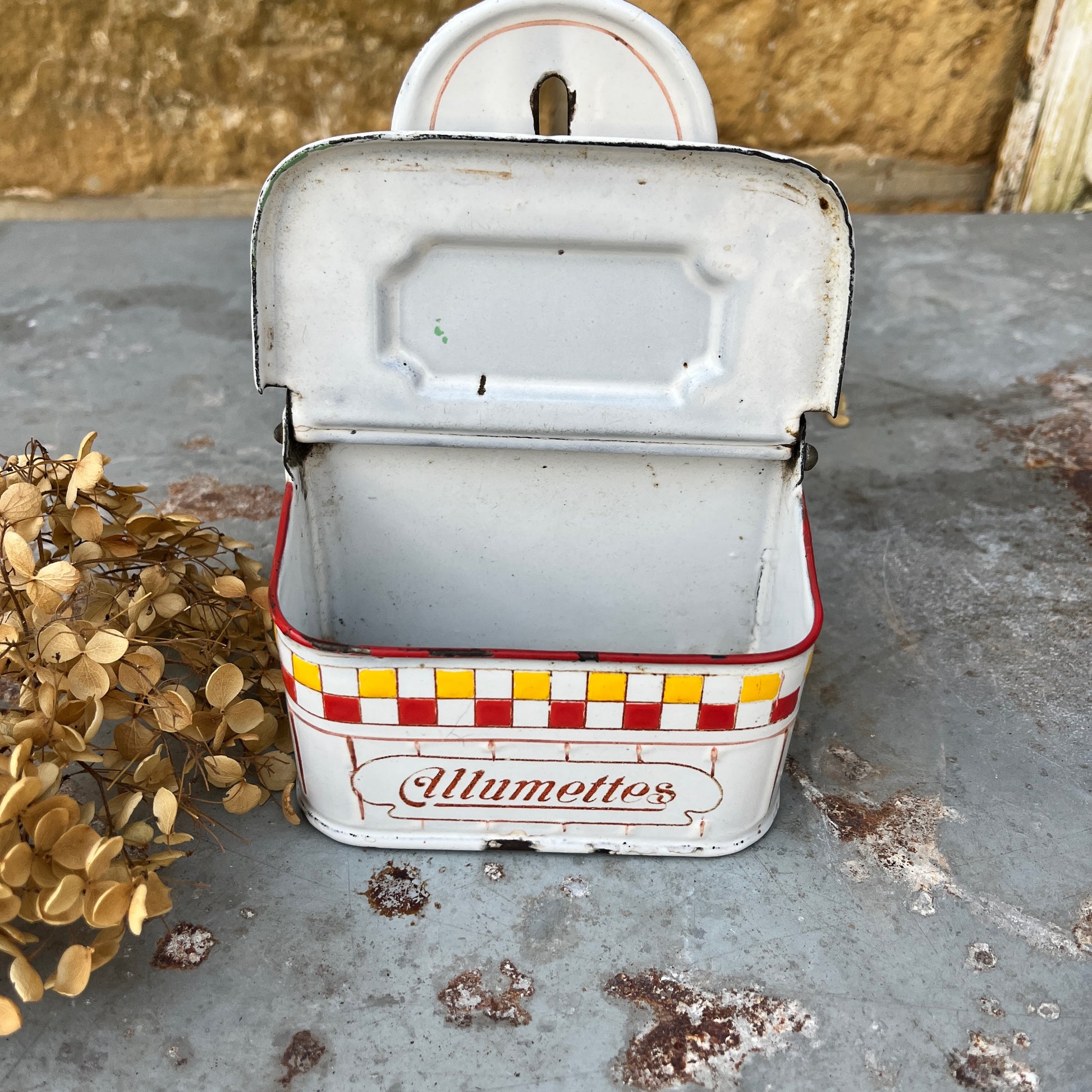 A vintage enamel allumettes box with a white background and red & yellow hand-painted geometric pattern, featuring a chippy weathered finish. The small, rectangular box has a hinged lid, exuding classic French charm