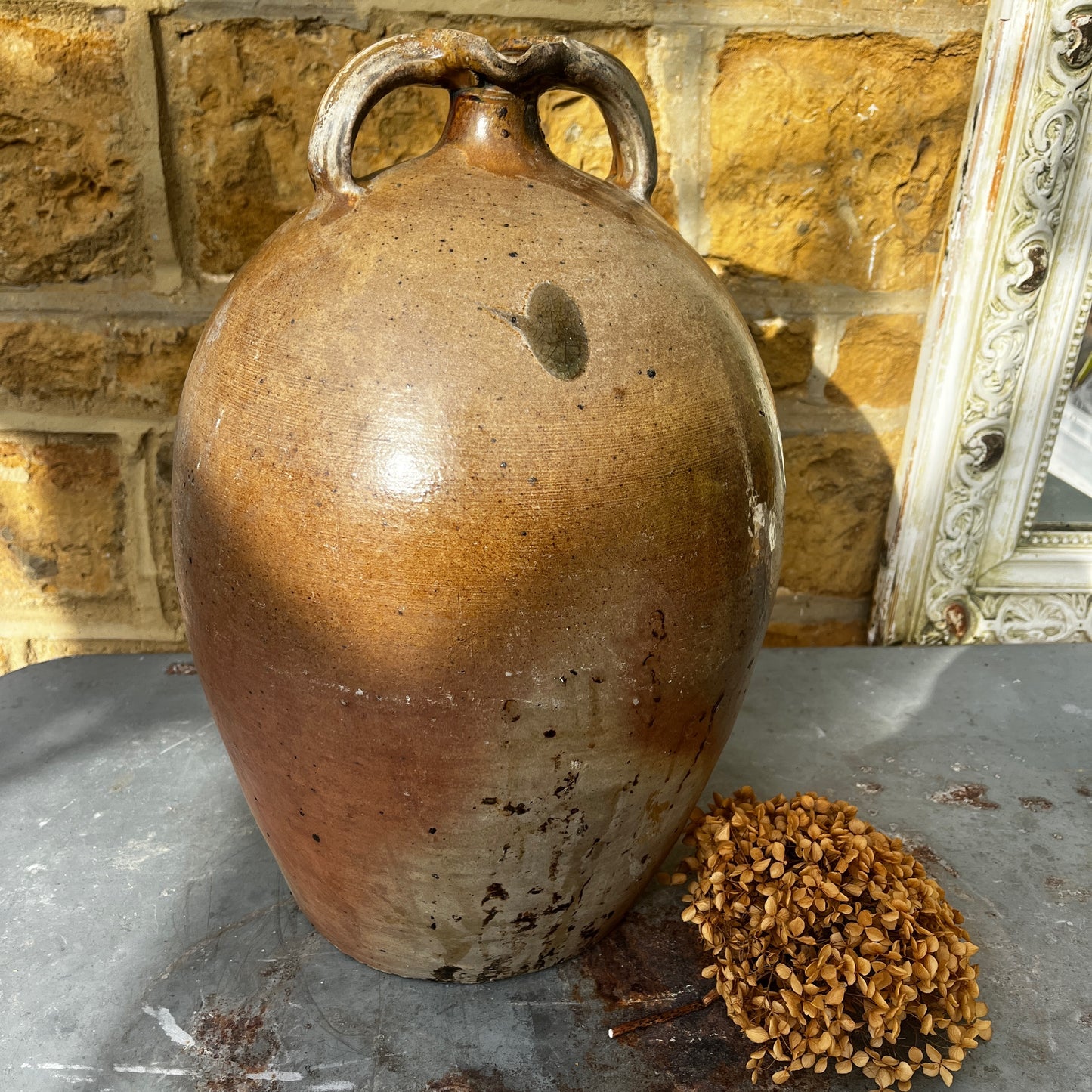 
Large vintage French stoneware oil jar with a rounded body, narrow neck, and earthy glaze, showing natural patina and rustic texture typical of traditional French farmhouse pottery.
