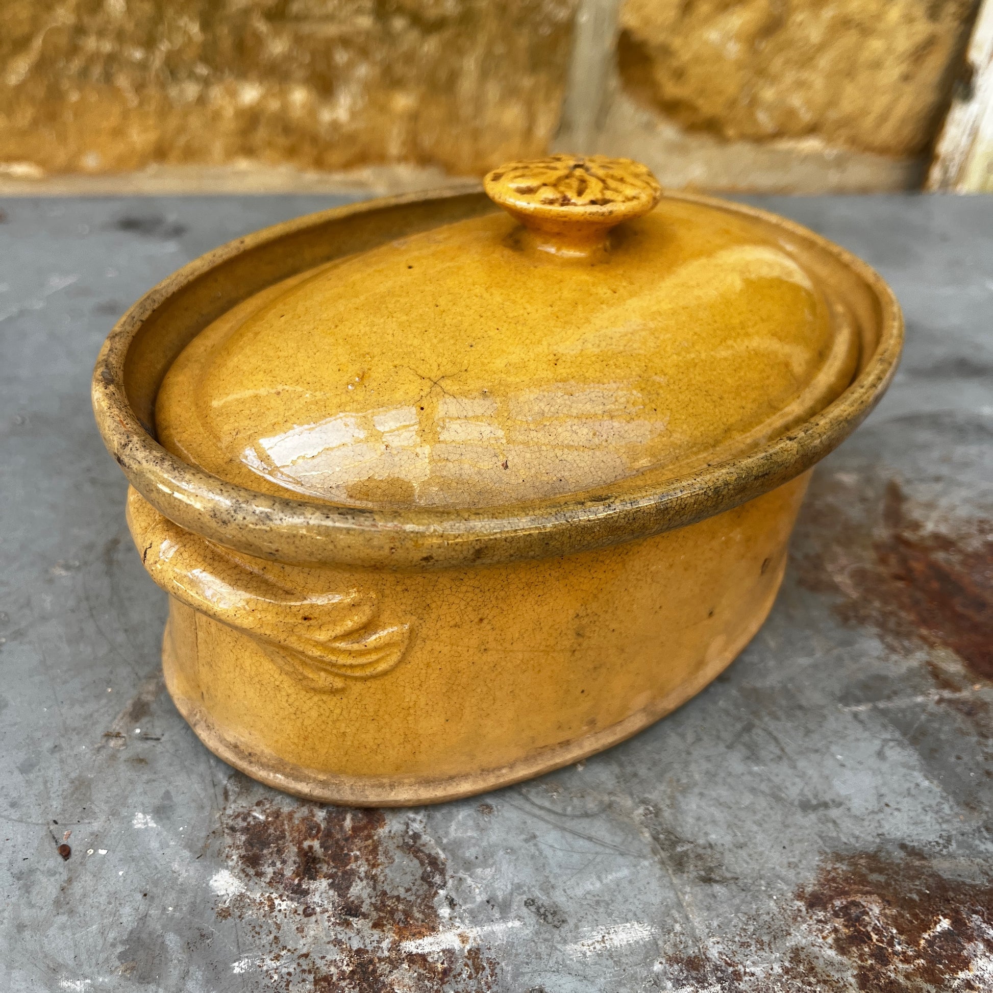 A small oval ceramic lidded french tureen dish in a warm mustard-yellow glazed finish.