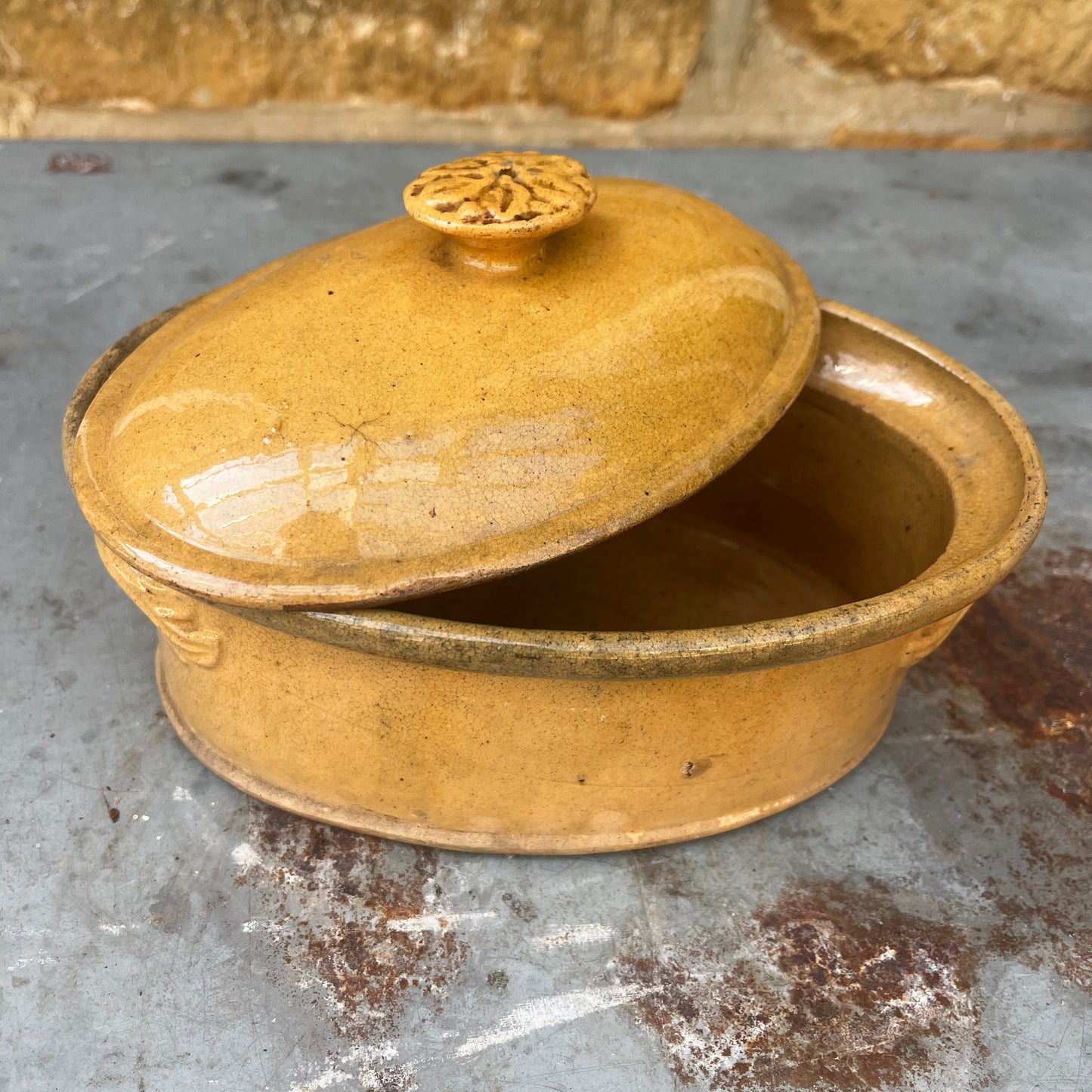 A small oval ceramic lidded french tureen dish in a warm mustard-yellow glazed finish.