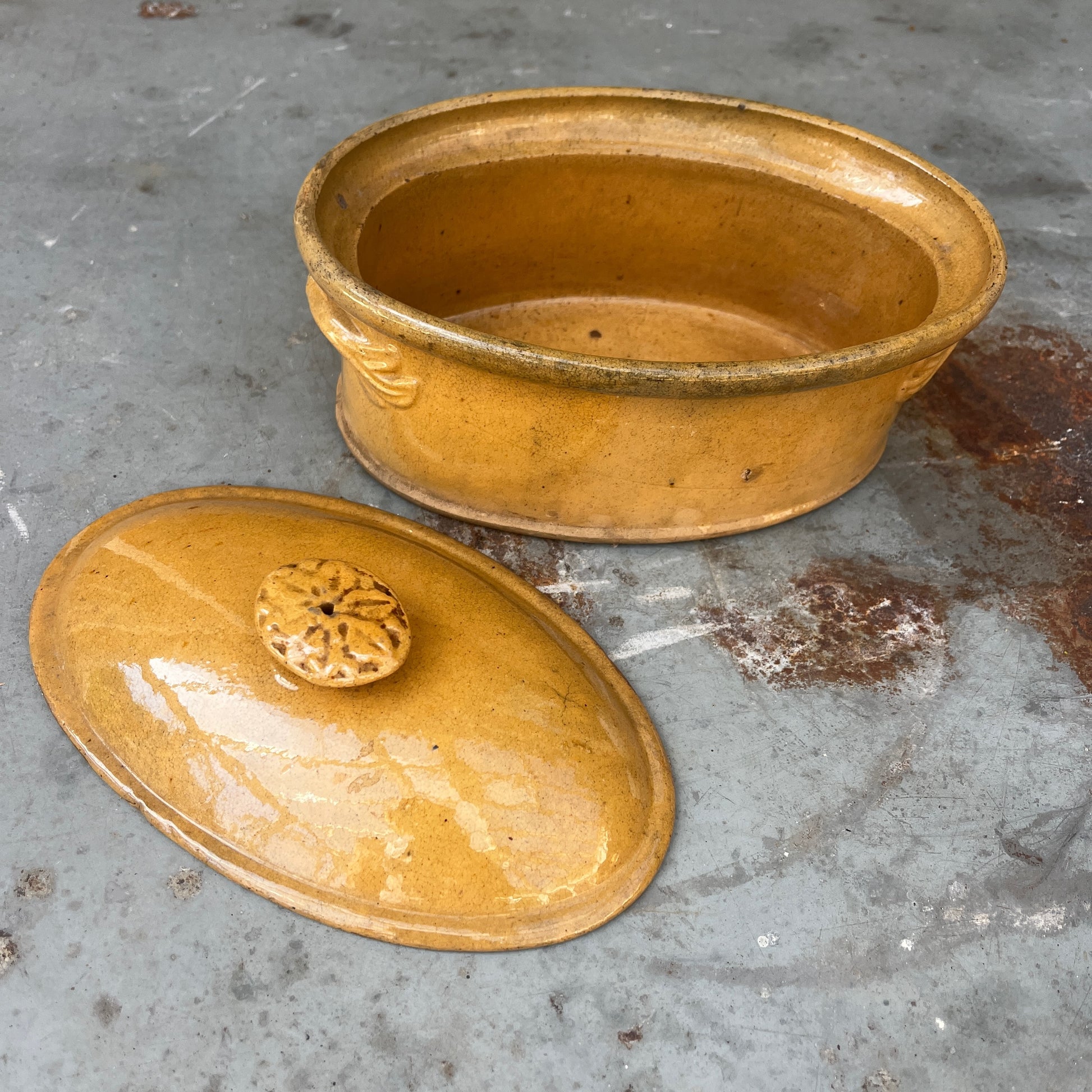 A small oval ceramic lidded french tureen dish in a warm mustard-yellow glazed finish.