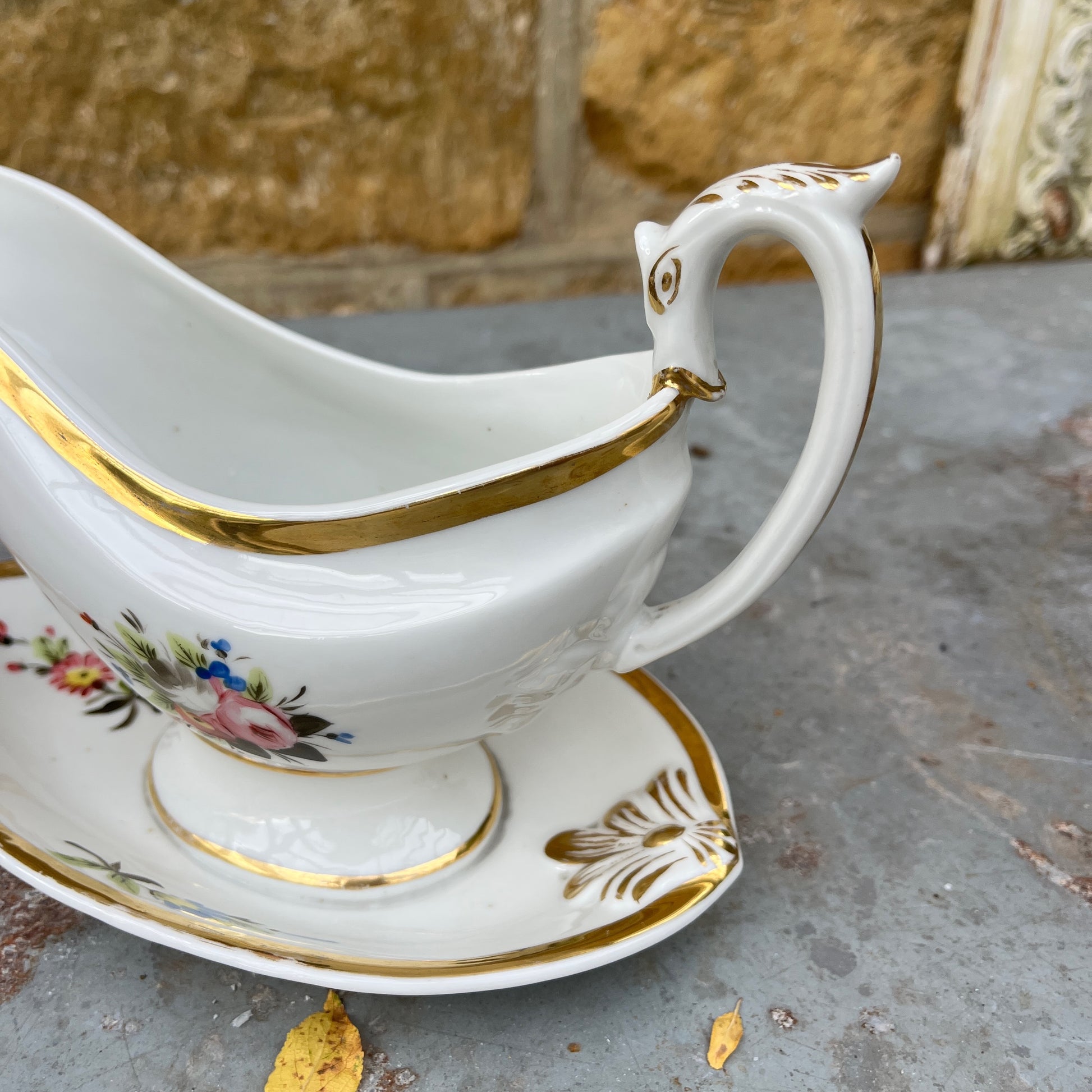 French vintage sauce boat with a fixed saucer, decorated with delicate hand-painted floral motifs and gilded accents along the edges. The piece has an elegant, classic design reflecting refined French tableware style.