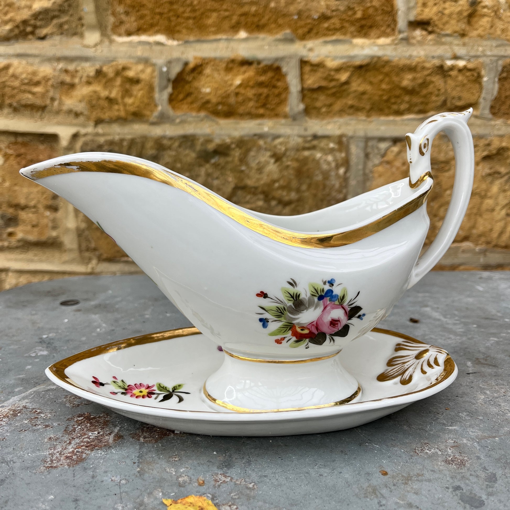 French vintage sauce boat with a fixed saucer, decorated with delicate hand-painted floral motifs and gilded accents along the edges. The piece has an elegant, classic design reflecting refined French tableware style.