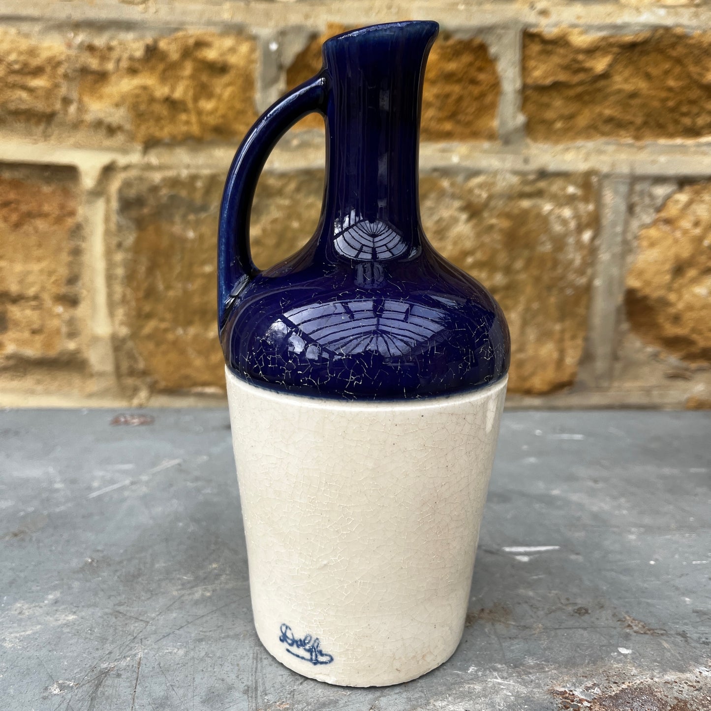 Ceramic pitcher with blue top and white base against a stone wall background