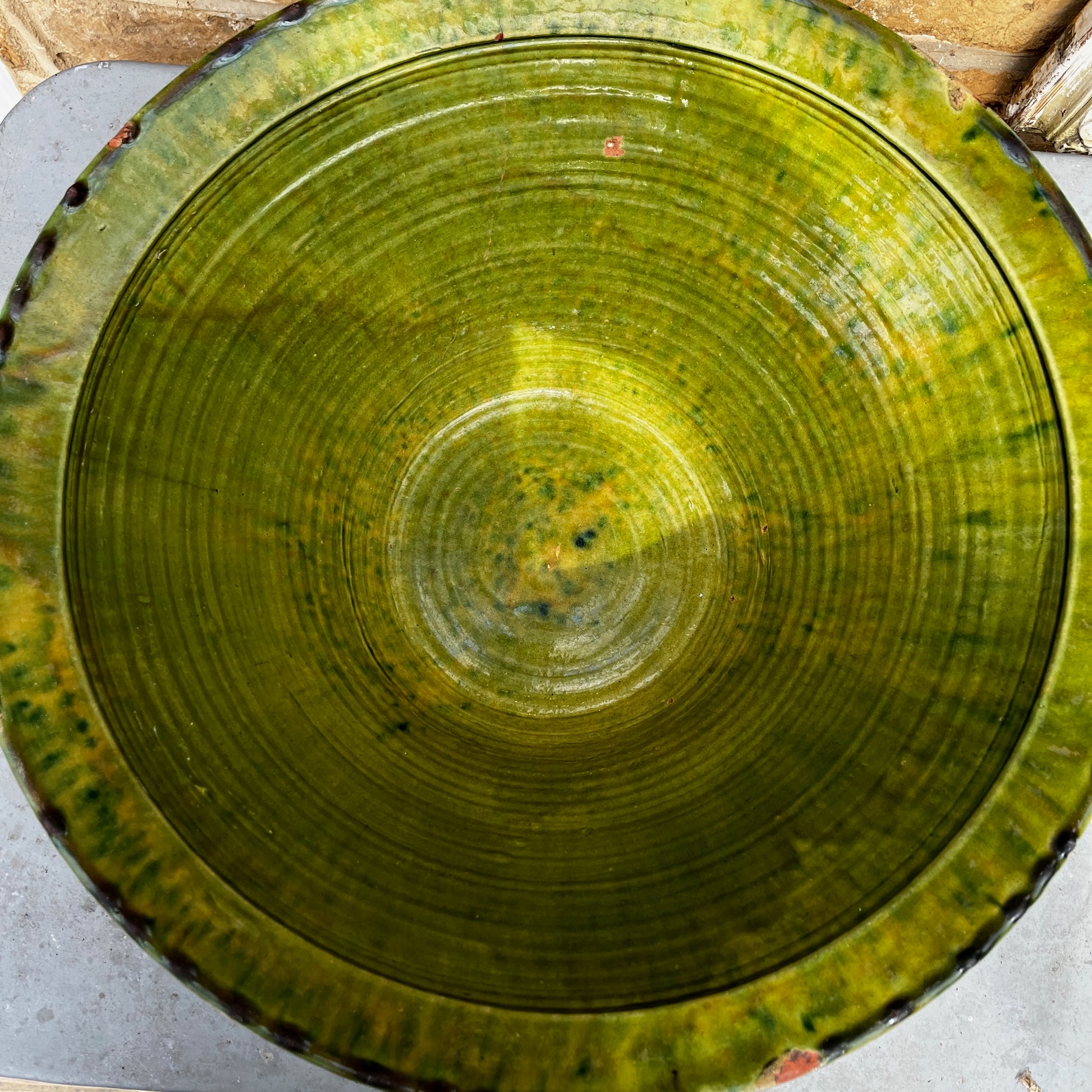 An 18th-century Tian bowl in glazed green earthenware with a simple, hand-crafted form and richly aged finish. The bowl features a wide, gently flared rim and a deep rounded shape, showcasing subtle variations in the green glaze that reflect its age and traditional craftsmanship