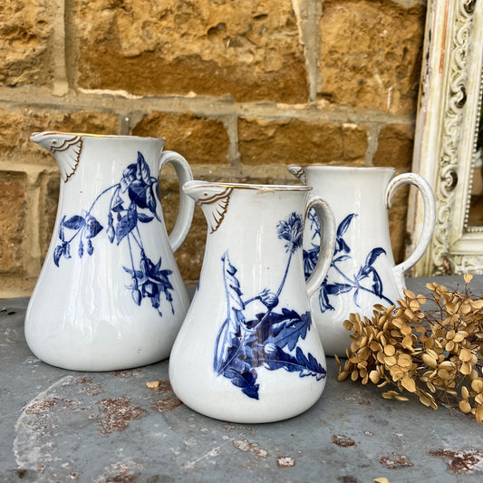 Three white ceramic vintage french jugs with blue floral patterns and gold detailing on the spout and rim.