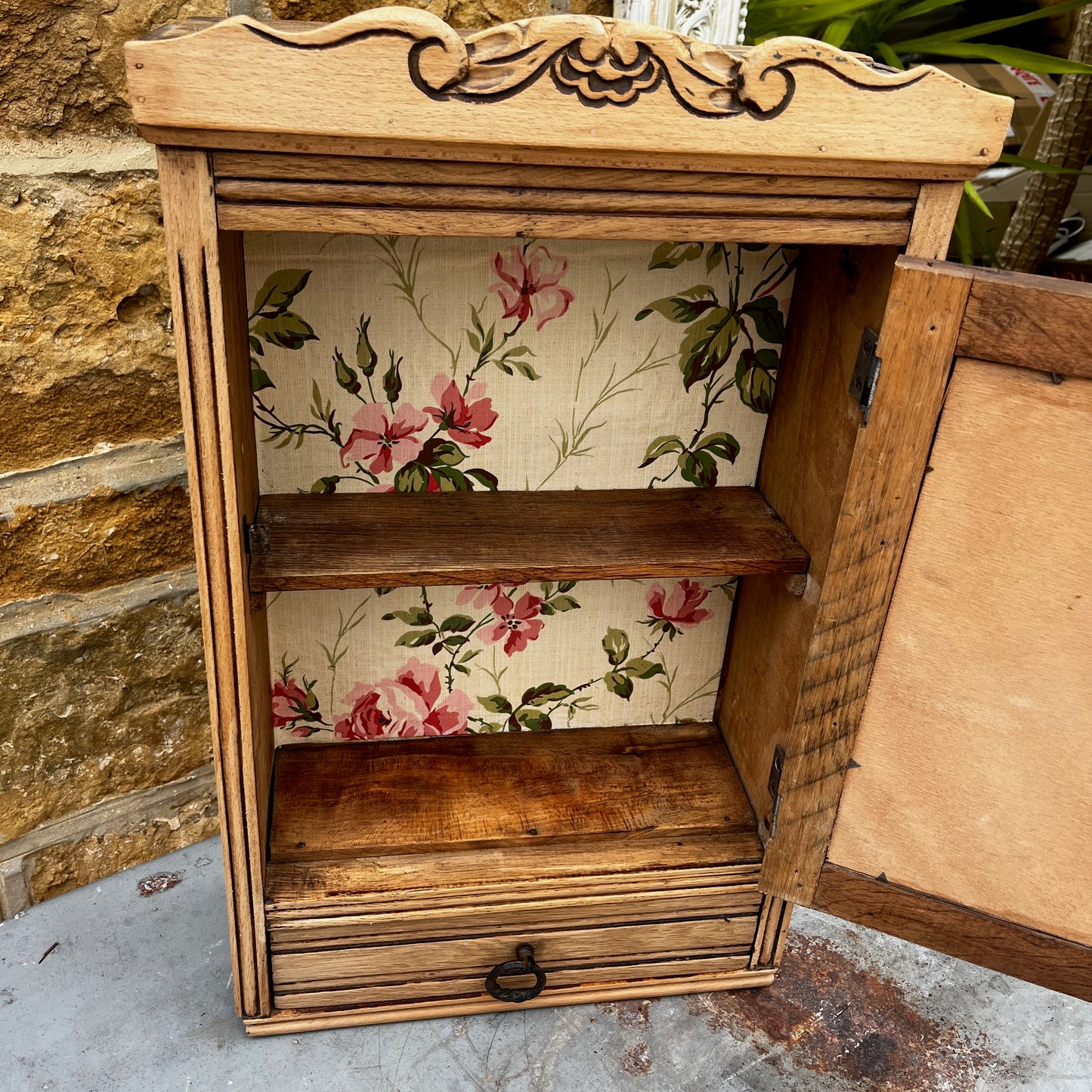 Vintage French wall cupboard with a mirrored door and a single drawer beneath. The interior of the cupboard and the base of the drawer are lined with decorative French paper, adding character and charm to the aged wooden piece.