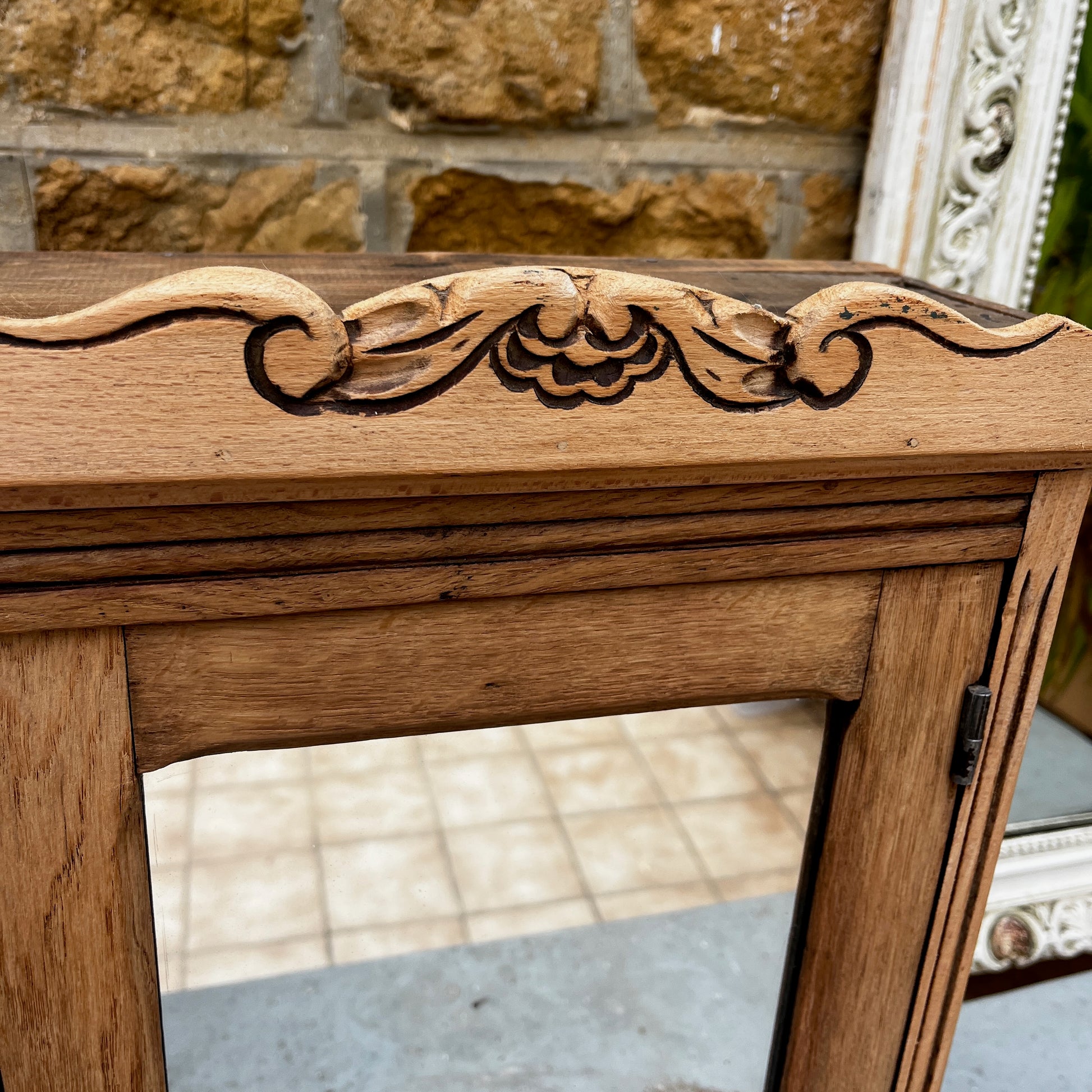 Vintage French wall cupboard with a mirrored door and a single drawer beneath. The interior of the cupboard and the base of the drawer are lined with decorative French paper, adding character and charm to the aged wooden piece.