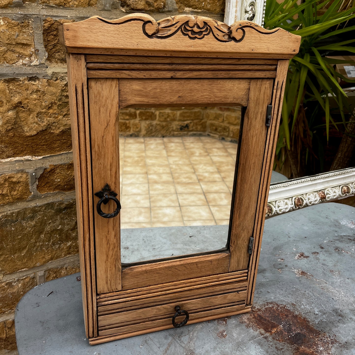 Vintage French wall cupboard with a mirrored door and a single drawer beneath. The interior of the cupboard and the base of the drawer are lined with decorative French paper, adding character and charm to the aged wooden piece.
