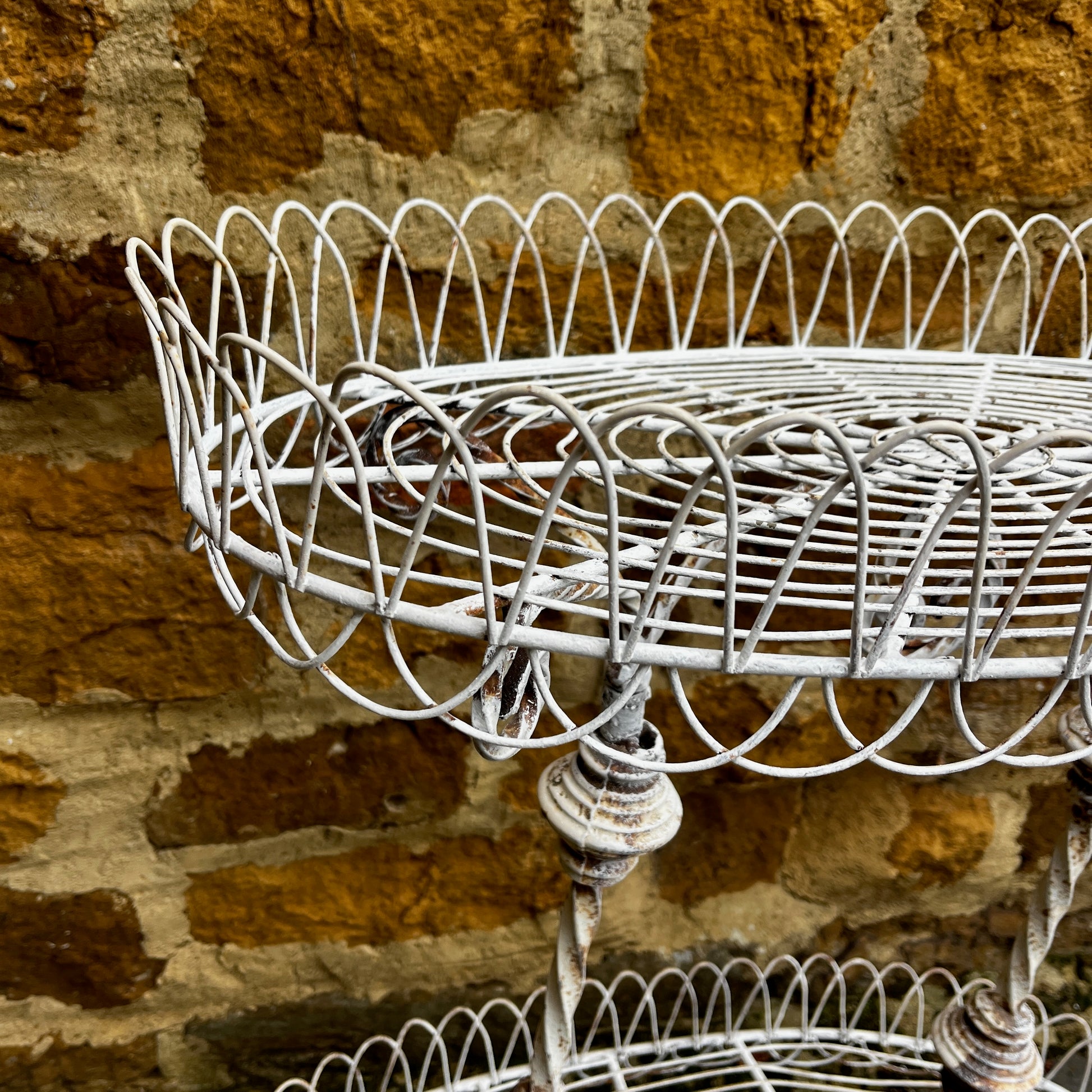 Two tier white vintage wire plant stand with two oval wire shelves with decorative scalloped edging.