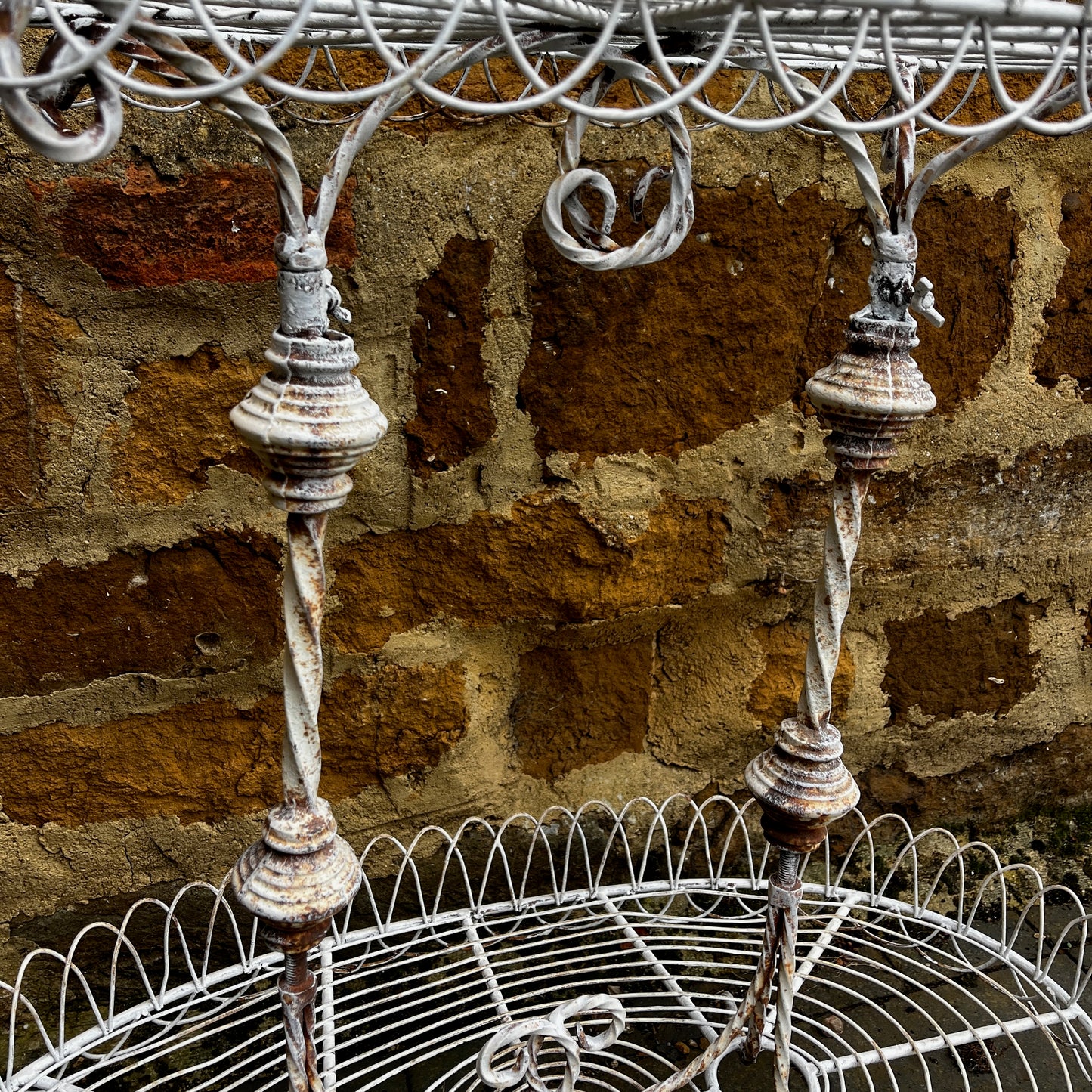 Two tier white vintage wire plant stand with two oval wire shelves with decorative scalloped edging.