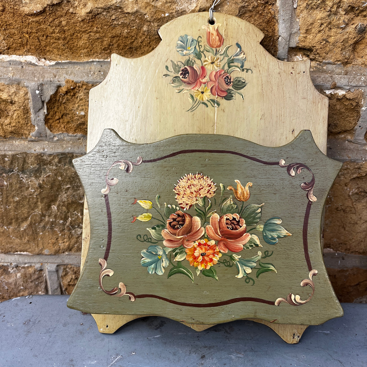 A vintage hand-painted wooden wall letter rack with a two-tone design, featuring a light natural wood top section and a muted sage green bottom section, both decorated with colorful floral motifs. 
