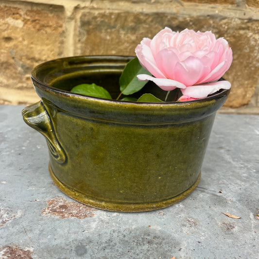 Green ceramic pot with a pink flower on a stone surface