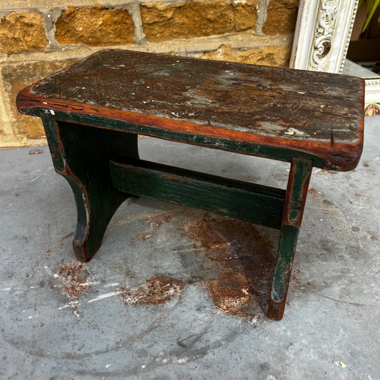 A vintage rustic wooden footstool with a beautifully worn green painted finish and a heavily distressed natural wood top.