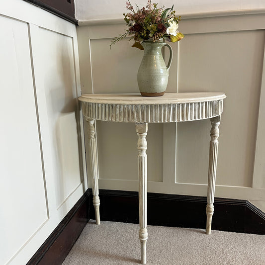 A Gustavian-style console table with a graceful, neoclassical design, featuring a distressed grey painted finish. The table has a demi-lune top supported by three elegantly curved legs