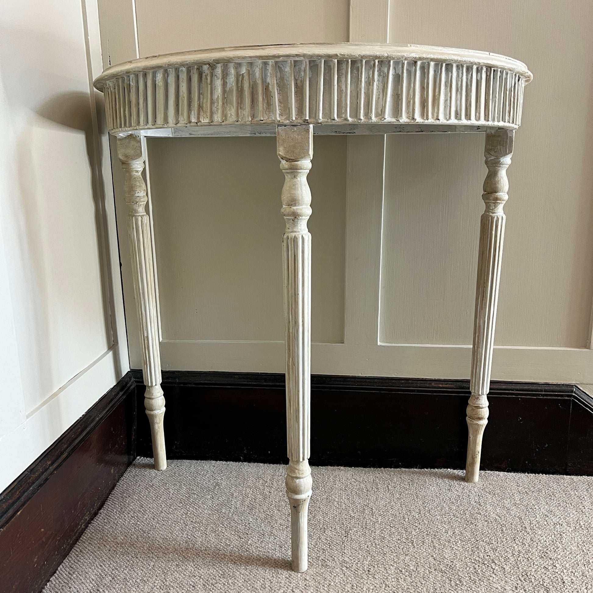 A Gustavian-style console table with a graceful, neoclassical design, featuring a distressed grey painted finish. The table has a demi-lune top supported by three elegantly curved legs
