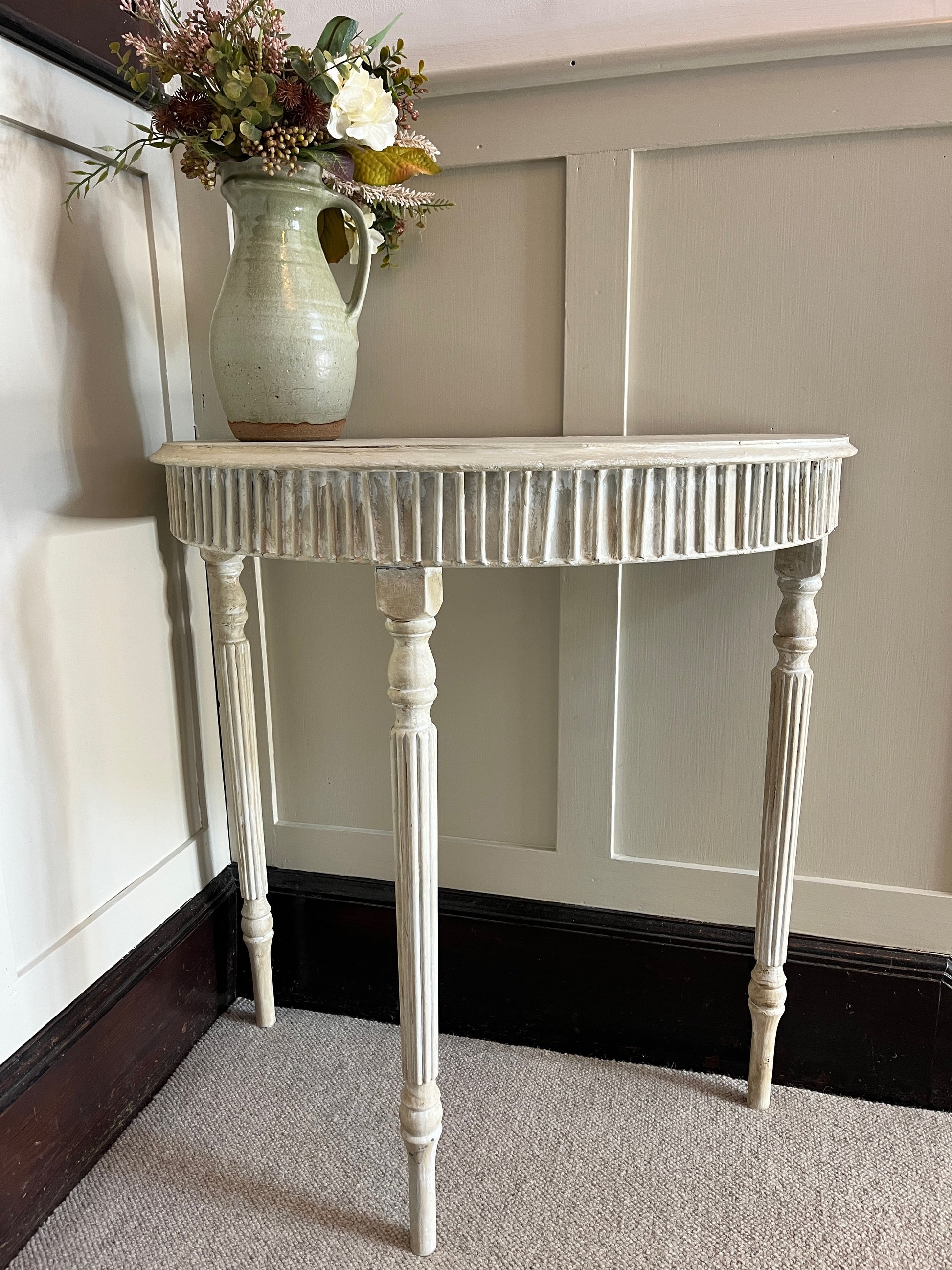 A Gustavian-style console table with a graceful, neoclassical design, featuring a distressed grey painted finish. The table has a demi-lune top supported by three elegantly curved legs