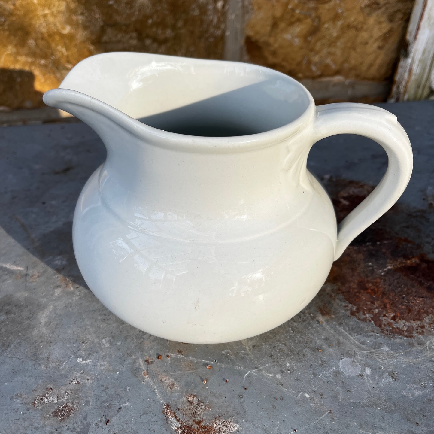 Simple French white ceramic jug with a rounded body, curved handle, and minimalist glazed finish in a classic utilitarian style.